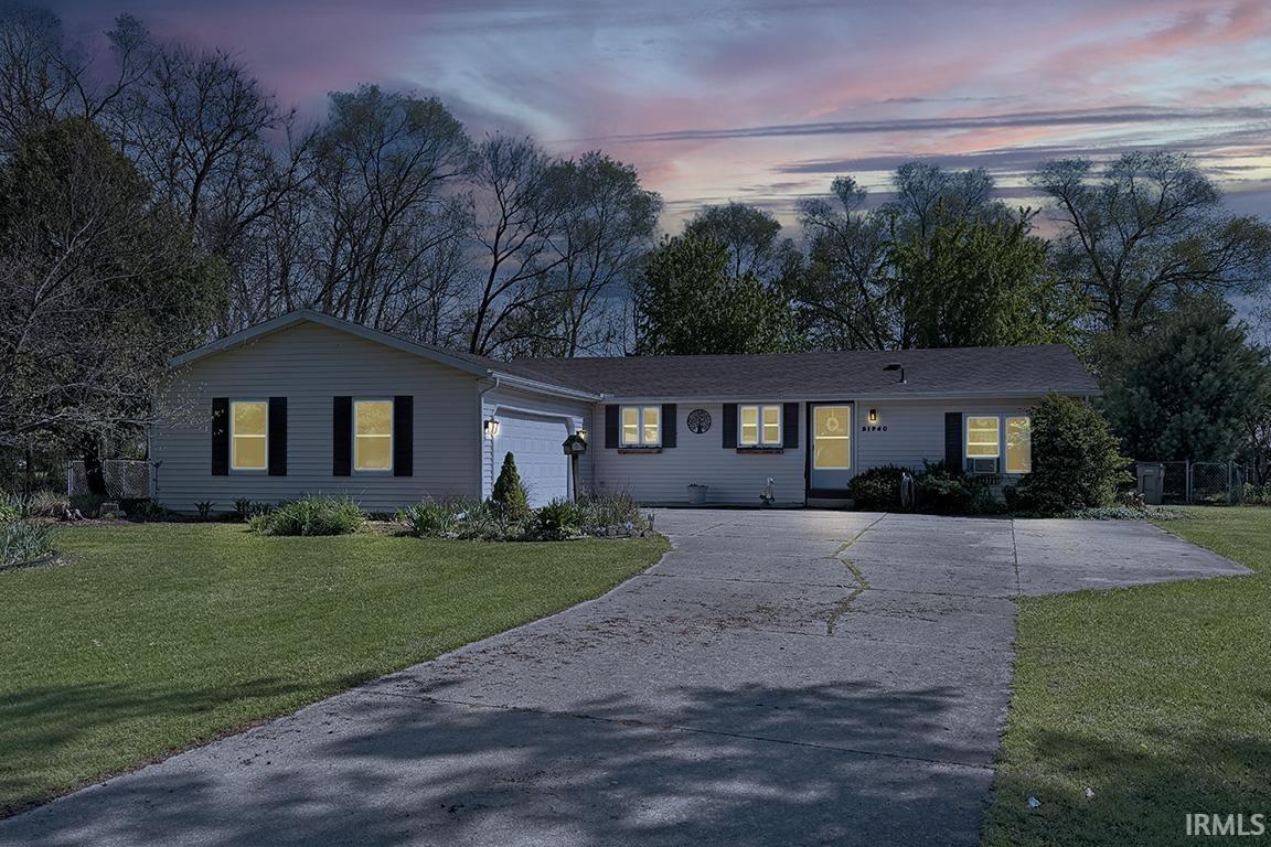 Ranch-style residence featuring light-colored siding, dark window shutters, an attached garage, a paved driveway, and manicured front lawn
