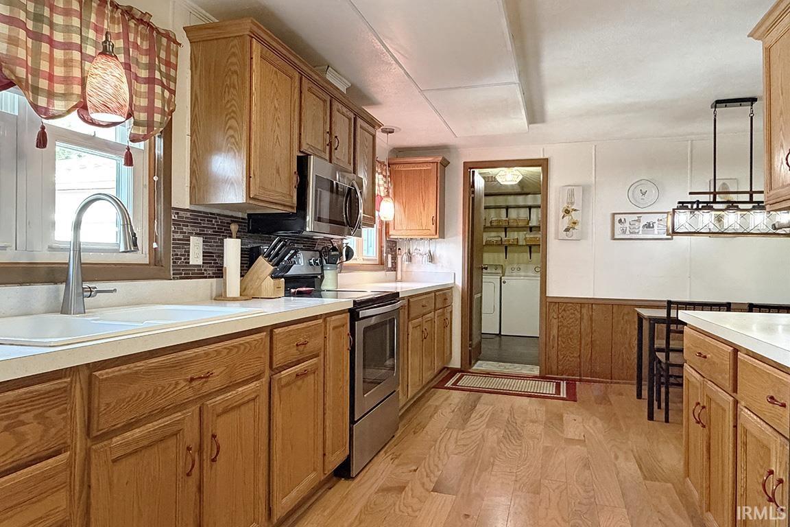 Kitchen featuring wood-finish flooring, oak cabinetry, stainless steel appliances, and a tiled backsplash