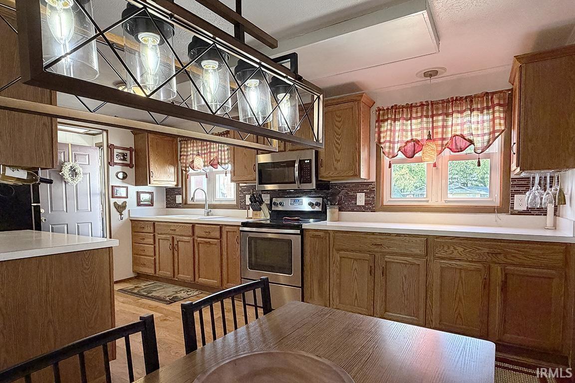 Kitchen featuring wood-finish cabinetry, white countertops, stainless steel appliances, and a tiled backsplash