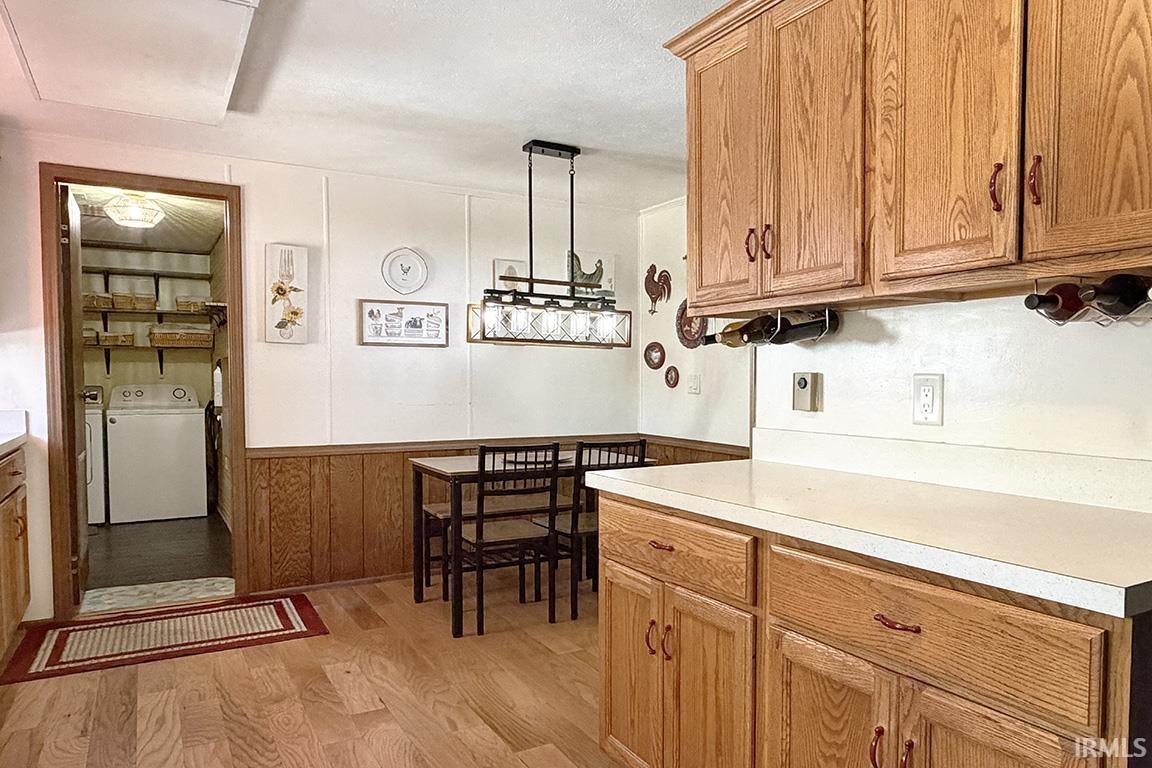 Kitchen with wood-finish flooring, wood cabinetry, light-toned countertops, and a dining area with a linear pendant light fixture