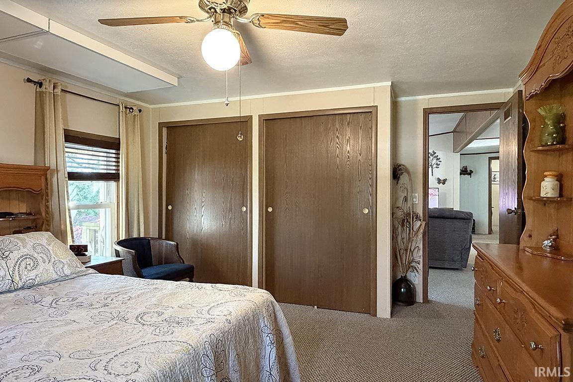 Carpeted room featuring two wood-finish bi-fold closet doors, a window with blinds and drapes, and a ceiling fan with light fixture