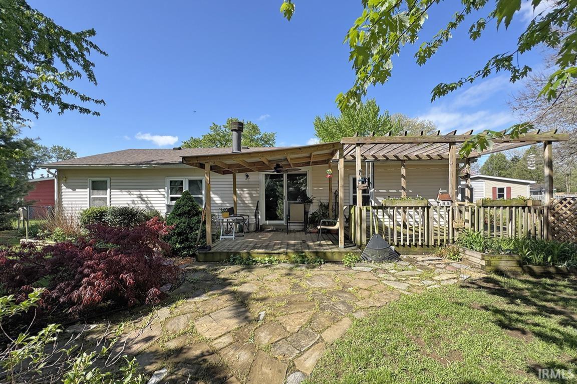 Rear exterior featuring a wooden deck with a pergola, stone patio, and mature landscaping