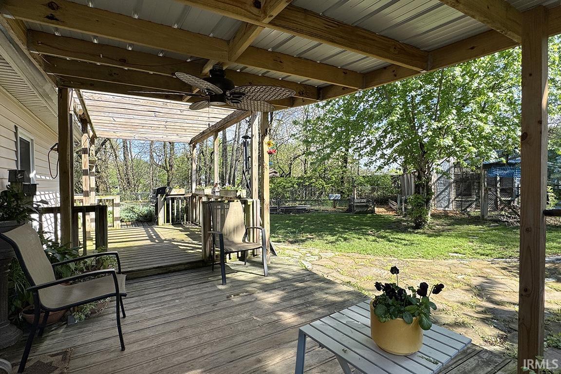 Expansive wood-finish deck with a covered patio area, featuring a ceiling fan, and an integrated pergola structure