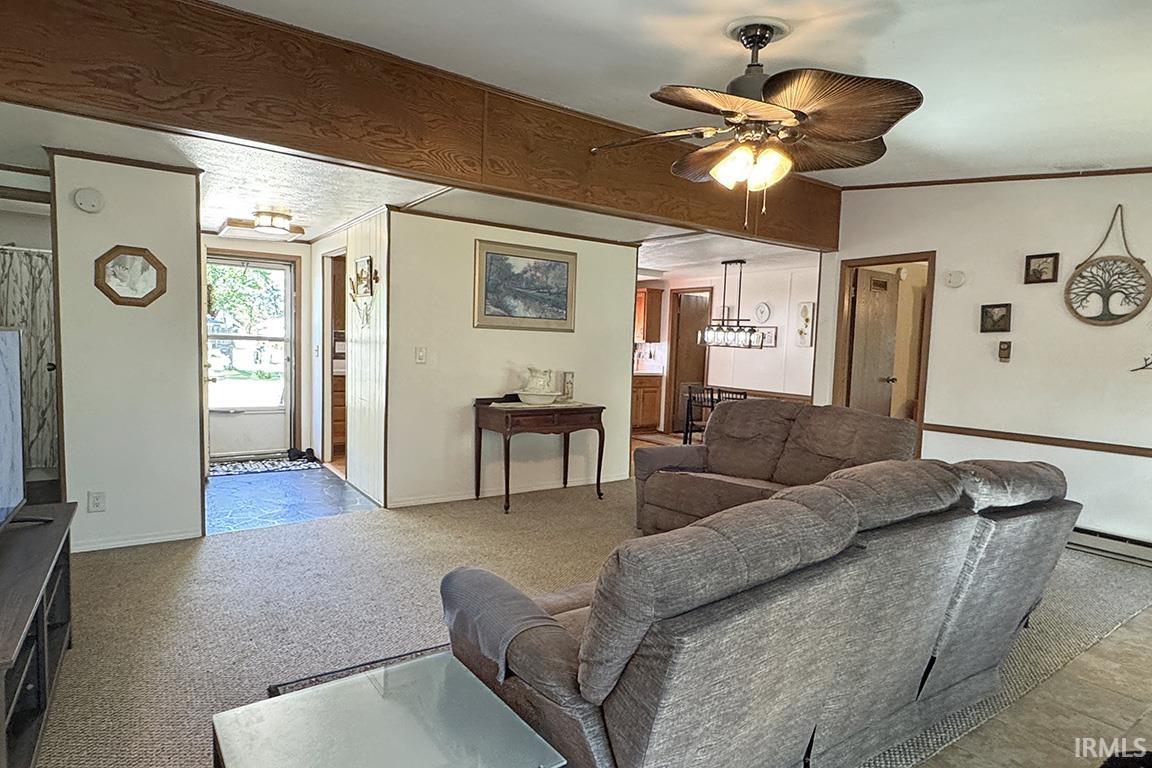 Carpeted living area featuring a decorative ceiling fan, white paneled walls, and wood-finish trim accents