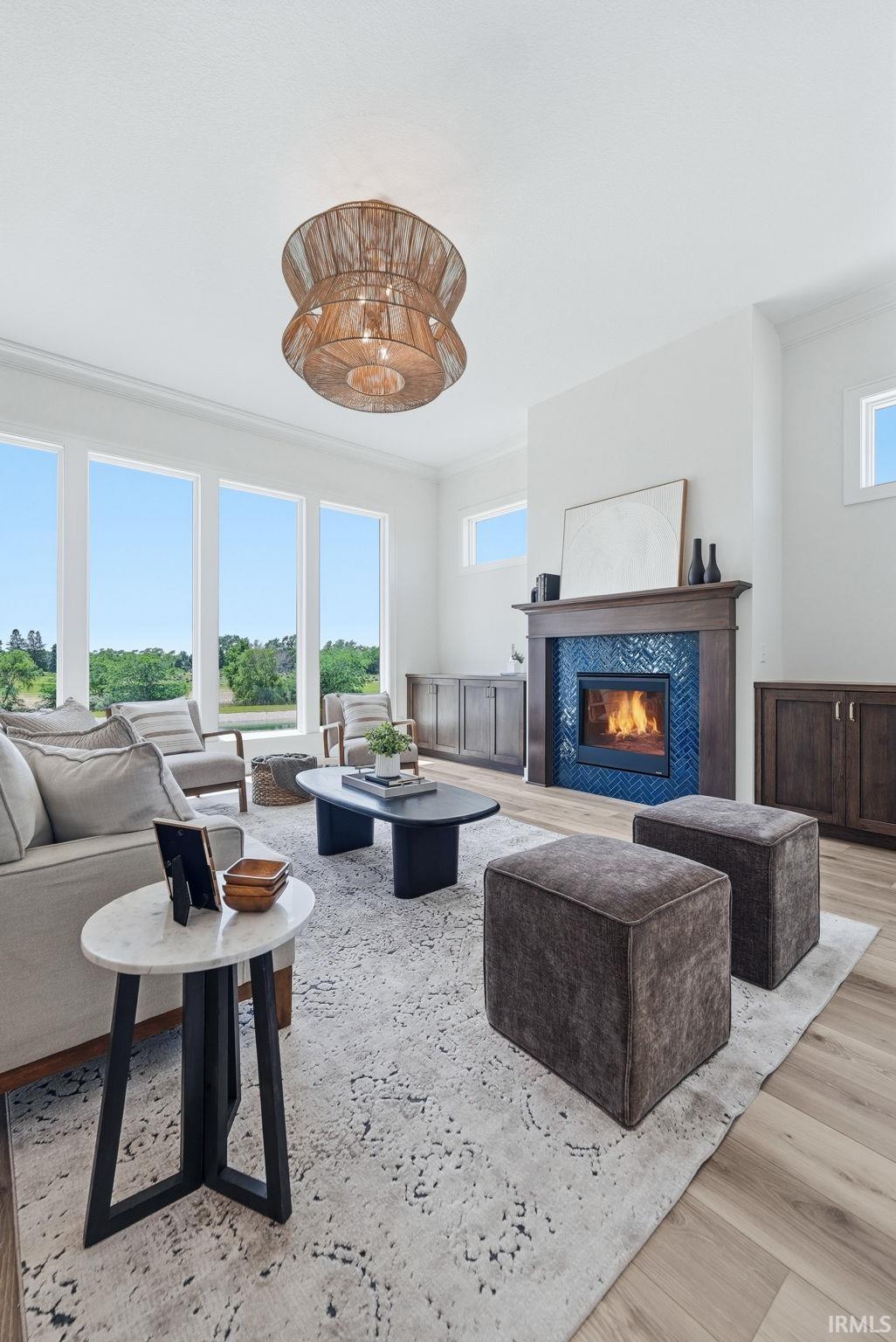 Spacious living area featuring large windows, wood-finish flooring, a contemporary fireplace with blue herringbone tile surround, a dark wood mantel, and built-in cabinetry
