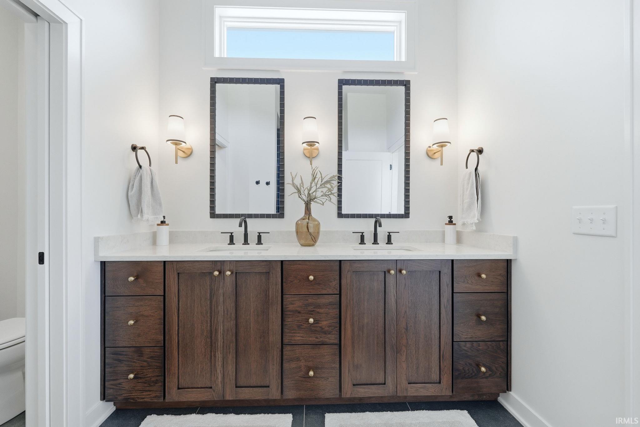 Double vanity featuring a light-colored countertop, dual undermount sinks with matte black faucets, and dark wood-finish cabinetry