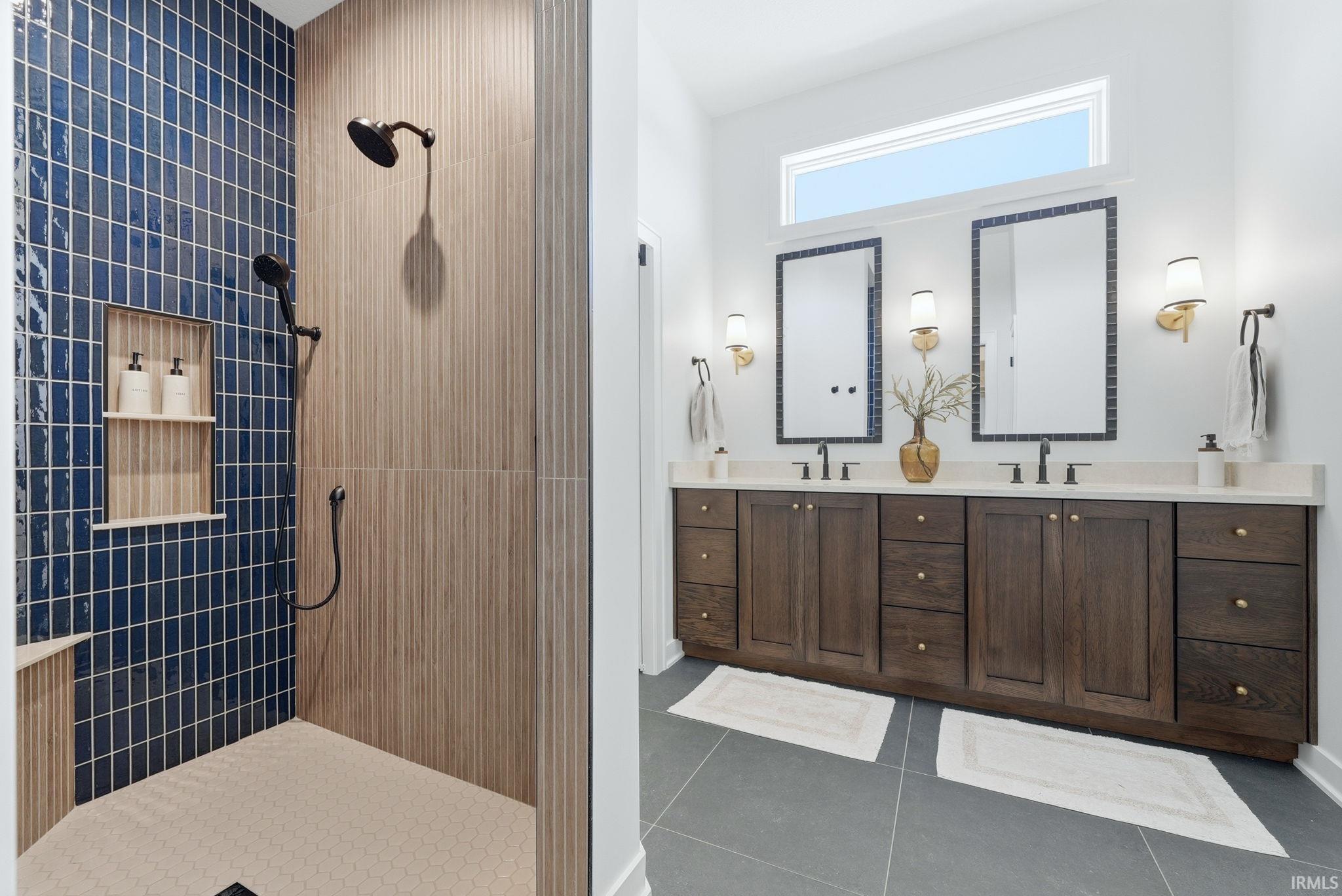 Bathroom featuring a shower with blue vertical subway tile and wood-finish accent walls, dual matte black shower heads, and a built-in shower niche