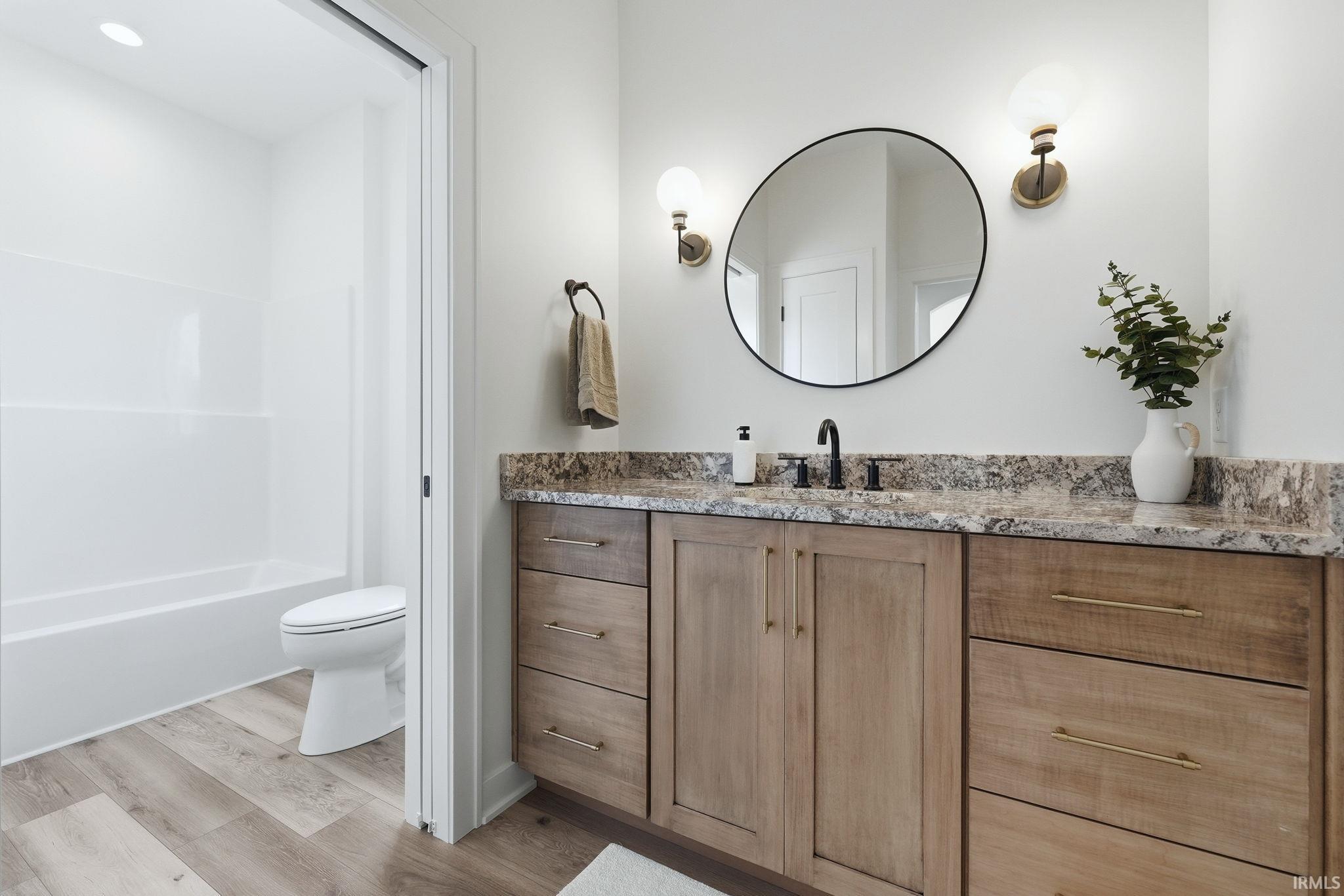 Bathroom featuring a dual-sink vanity with a stone countertop, wood-finish cabinetry, and a circular wall mirror