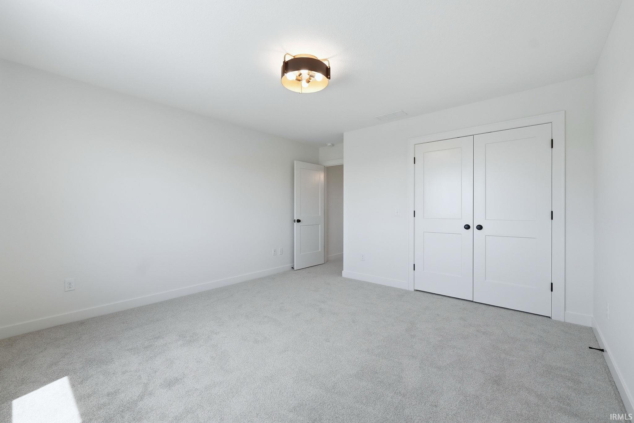 Room with neutral-toned carpeting, white walls, and a modern ceiling light fixture
