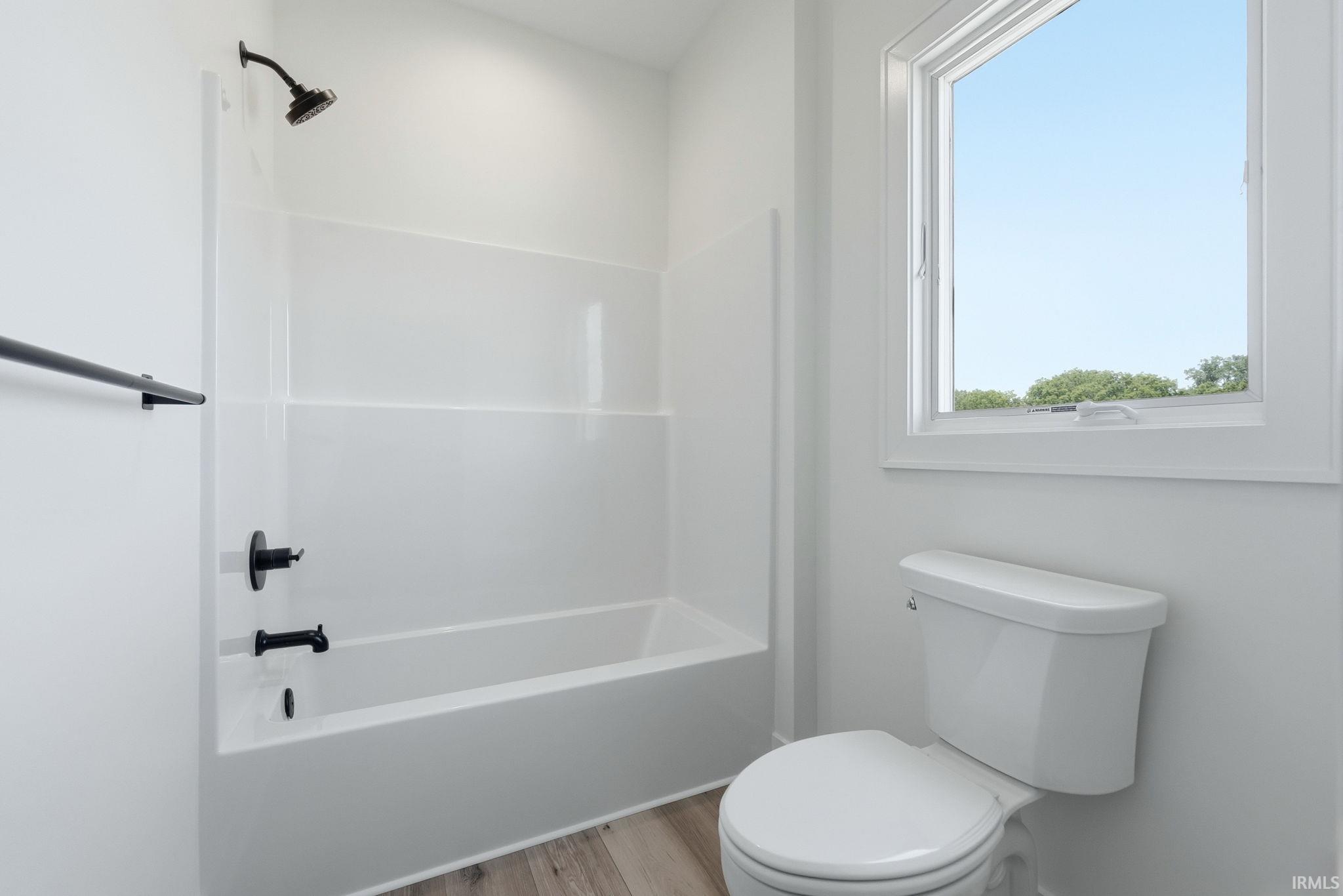 Full bathtub with a matte black showerhead and faucet, white shower surround, and a coordinating towel bar