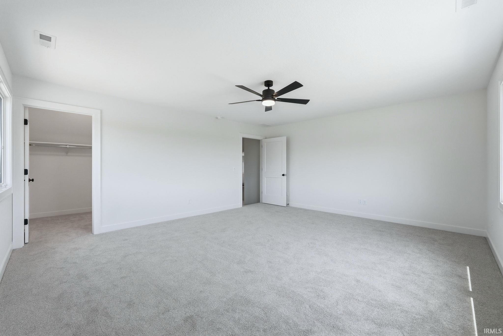Spacious room featuring light gray carpeting, crisp white walls, a contemporary ceiling fan, and ample natural light from the window