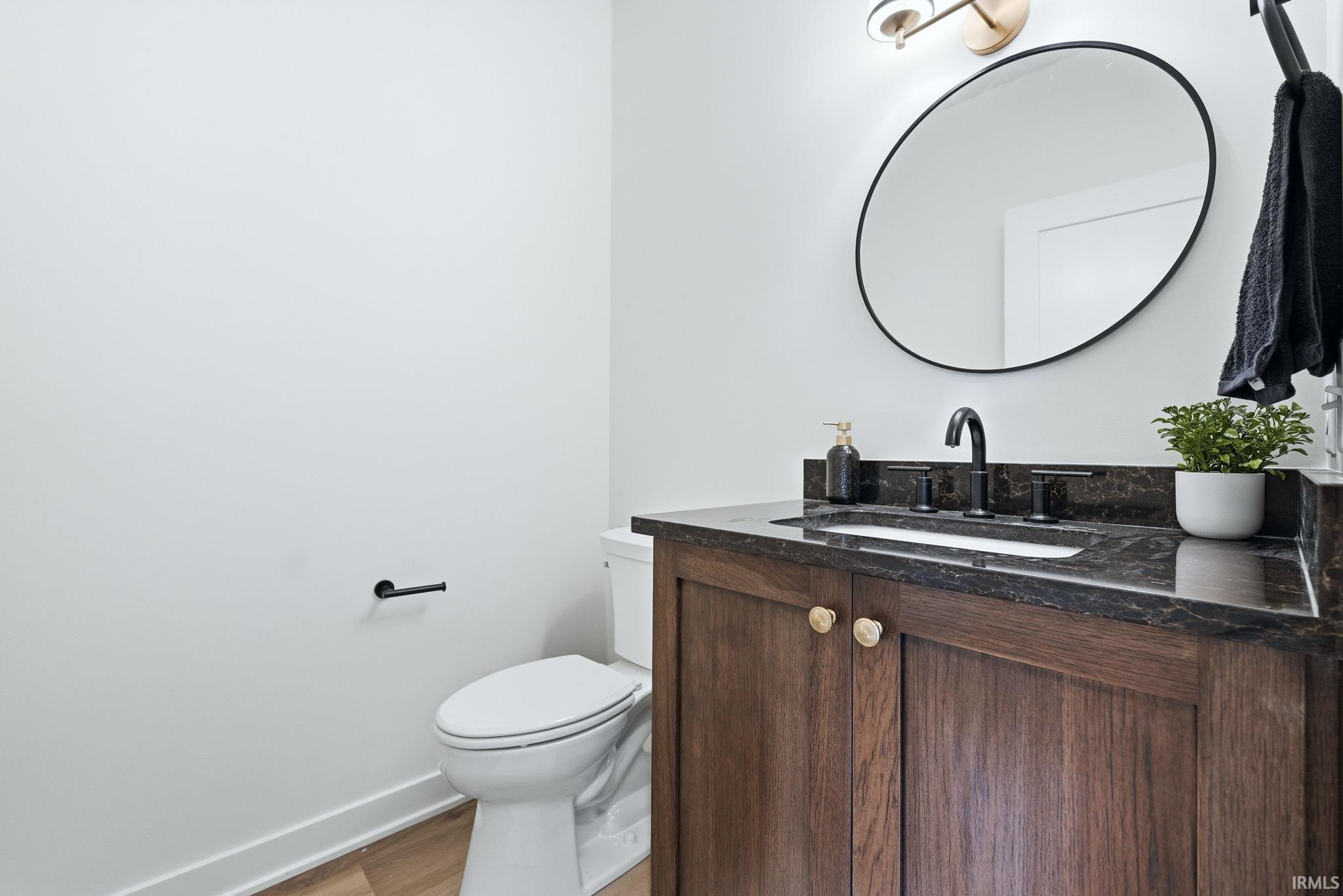 Vanity featuring a dark wood-finish cabinet with gold-toned hardware, a dark stone countertop, and an undermount sink