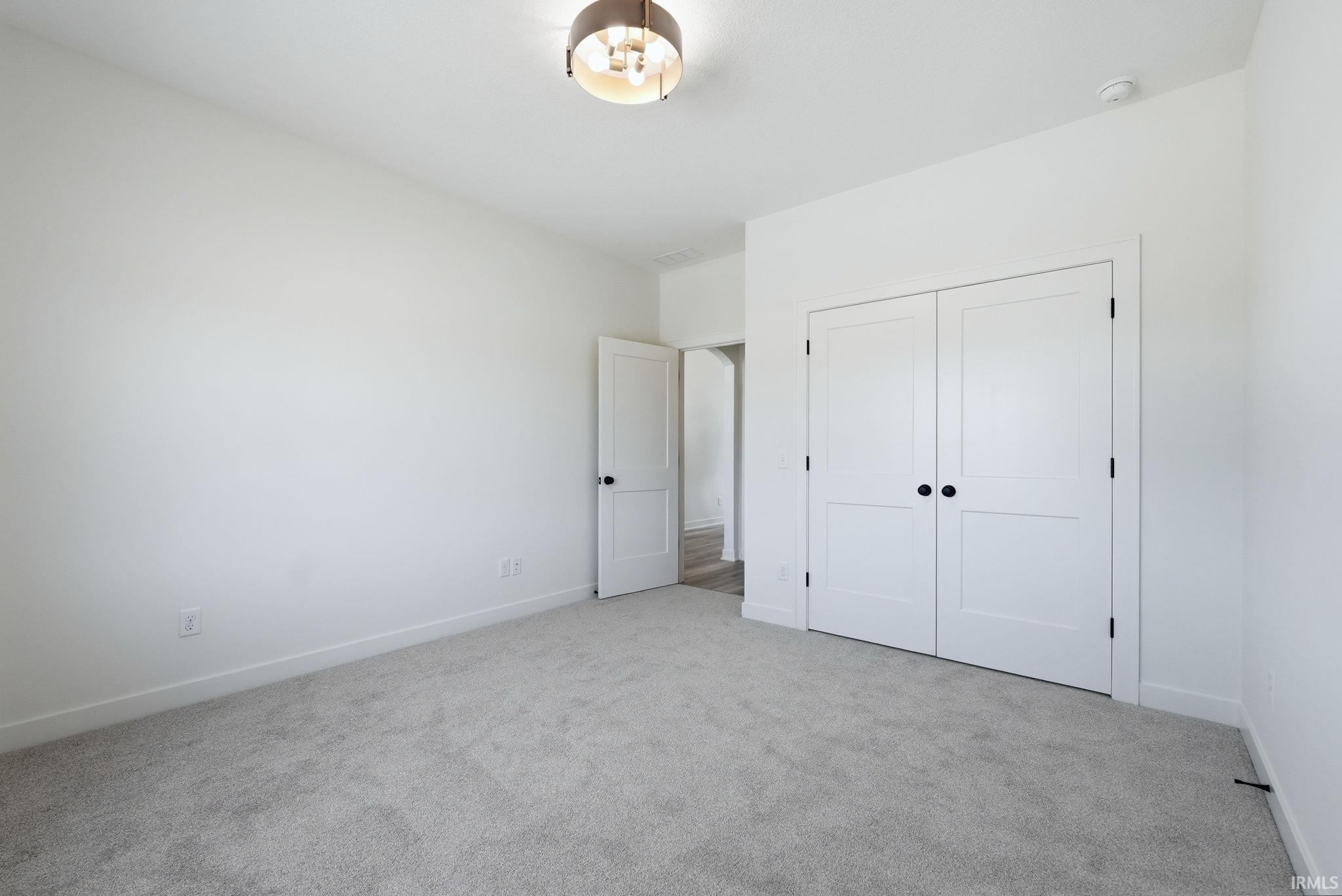 Neutral-toned carpeting paired with white walls, a white bi-fold closet door, and a white interior door