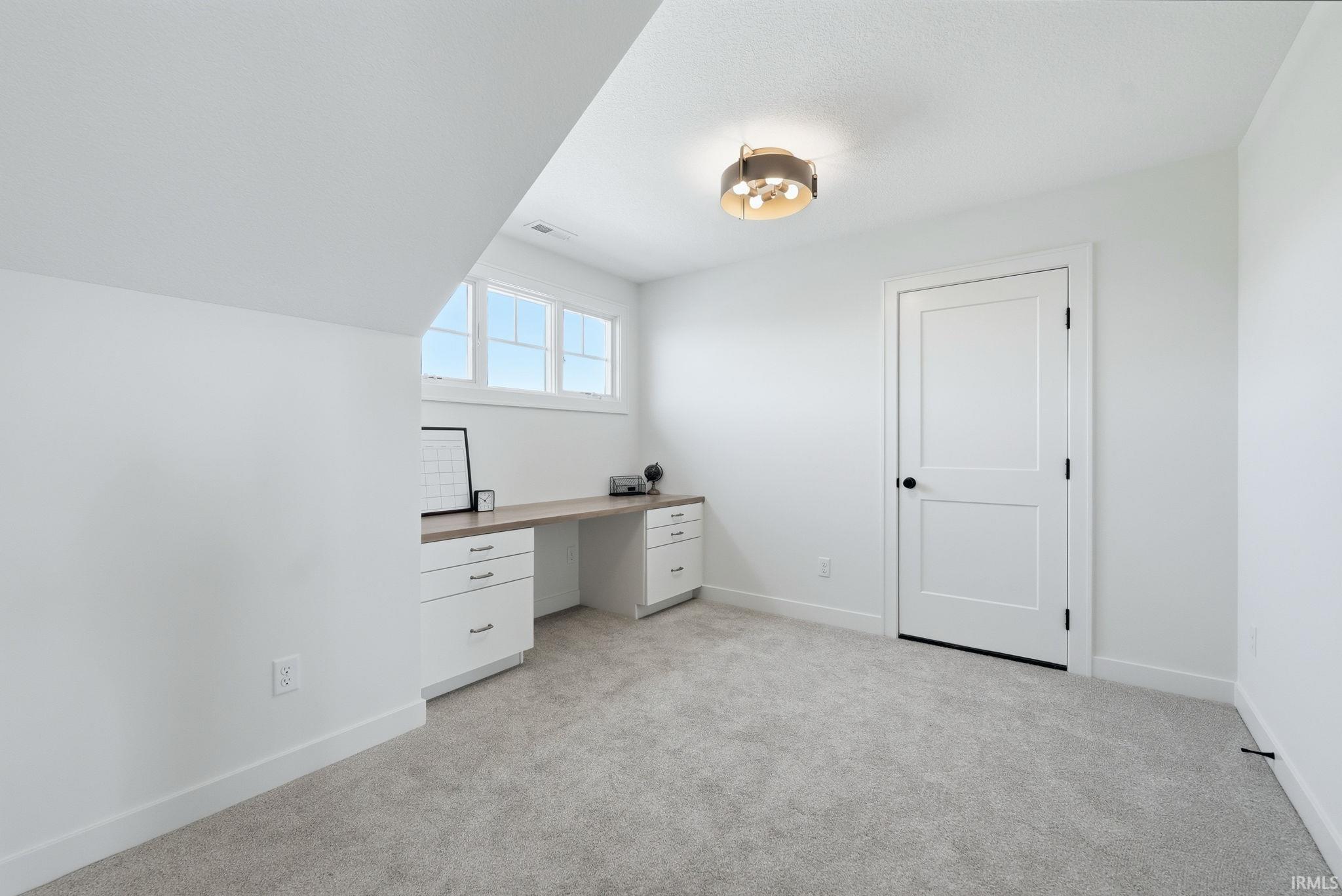 Carpeted room featuring a built-in desk with white cabinetry and a wood-finish countertop