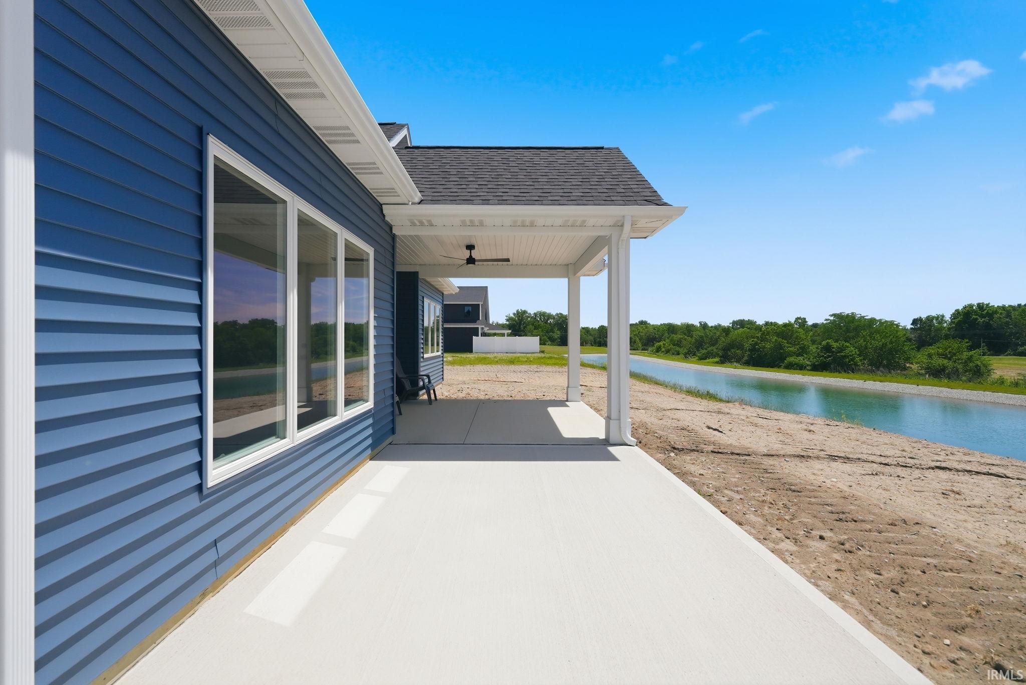 Spacious covered patio with concrete flooring, supported by white pillars, featuring a dark ceiling fan and offering expansive views of an adjacent waterway