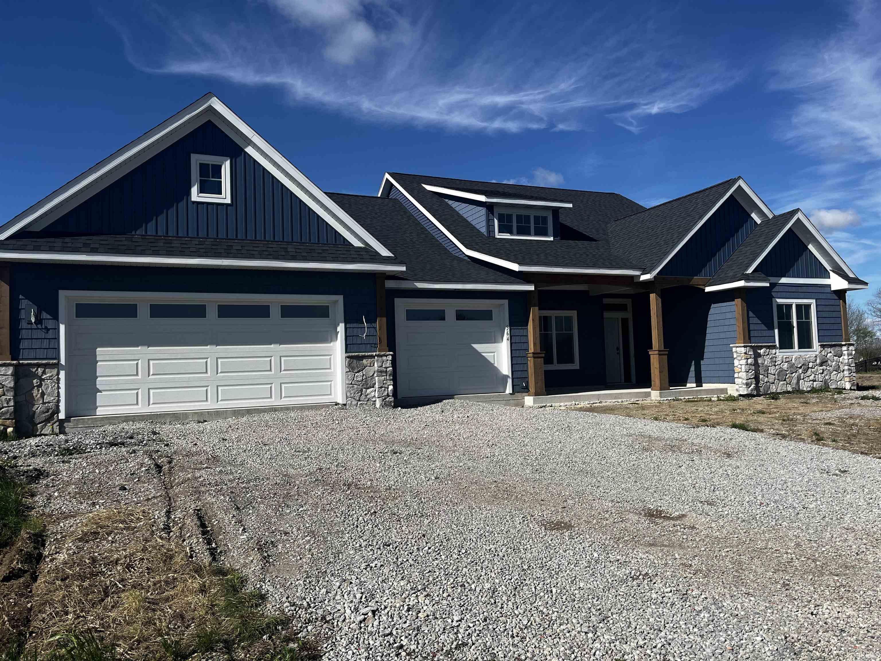 Deep blue siding exterior with stone accents, a multi-gabled roof, and two white garage doors