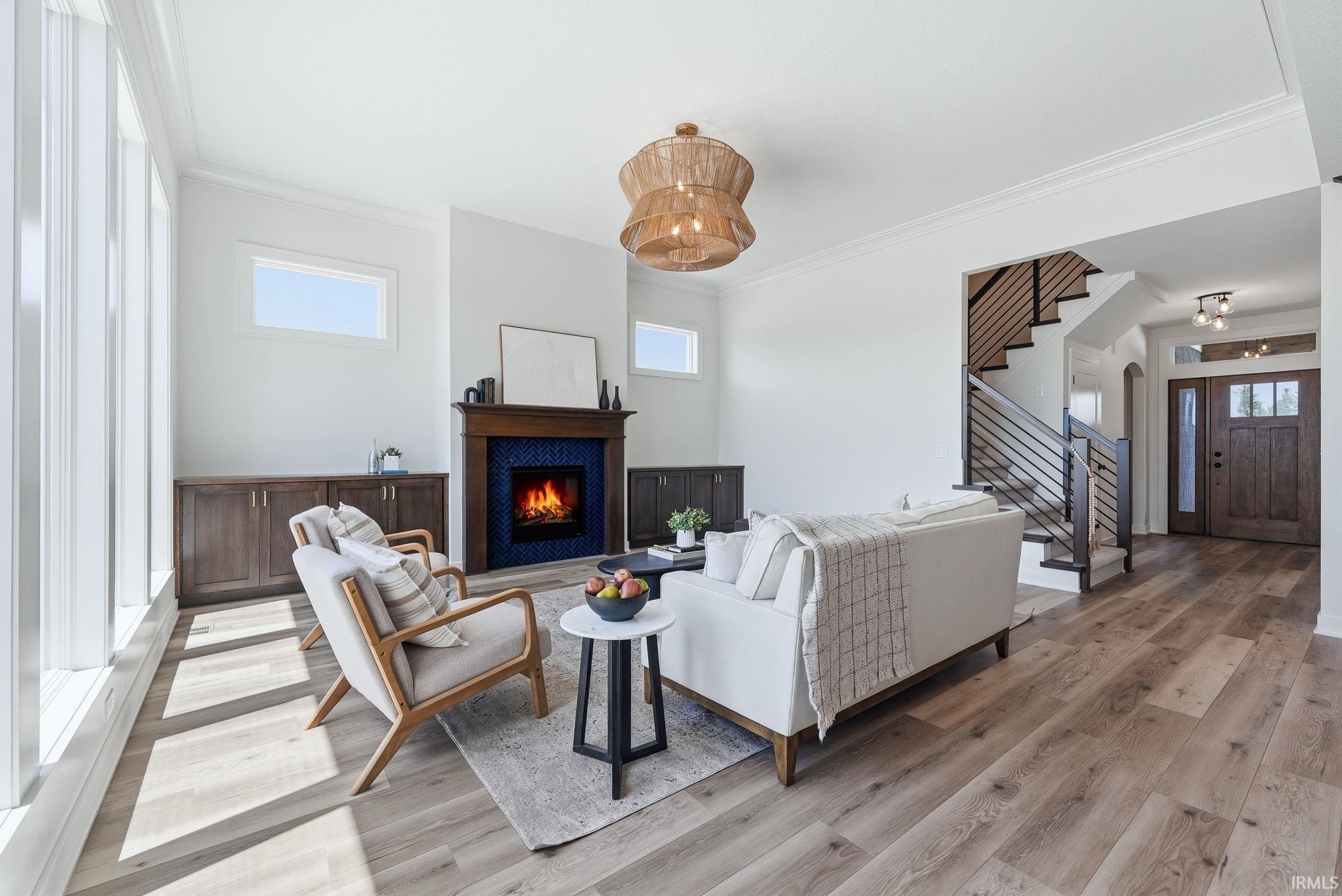 Open-concept living space featuring wood-finish flooring, a contemporary fireplace with blue tile surround and wood mantel, built-in cabinetry, and a prominent staircase with metal railings