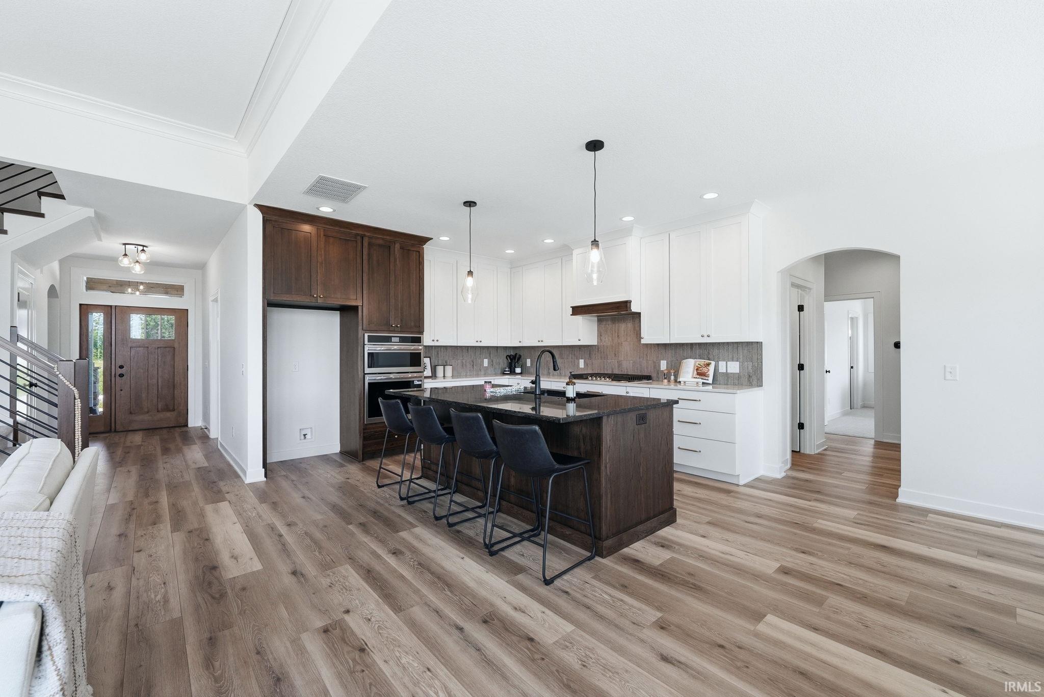 Kitchen featuring a dark wood-finish island, white upper and lower cabinetry, built-in double oven, and a tile backsplash