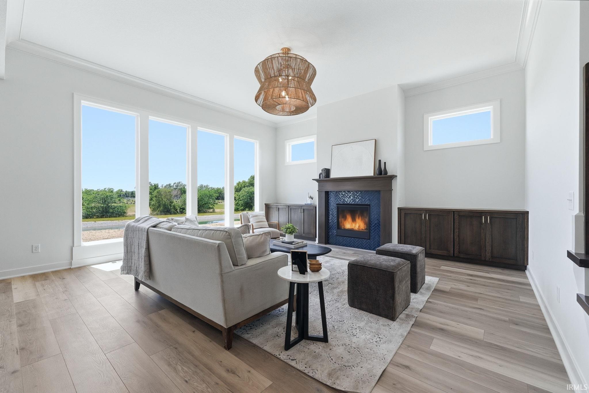 Spacious living area featuring expansive windows, wood-finish flooring, a contemporary fireplace with blue tile surround and dark wood mantel, built-in cabinetry, and a distinctive ceiling fixture