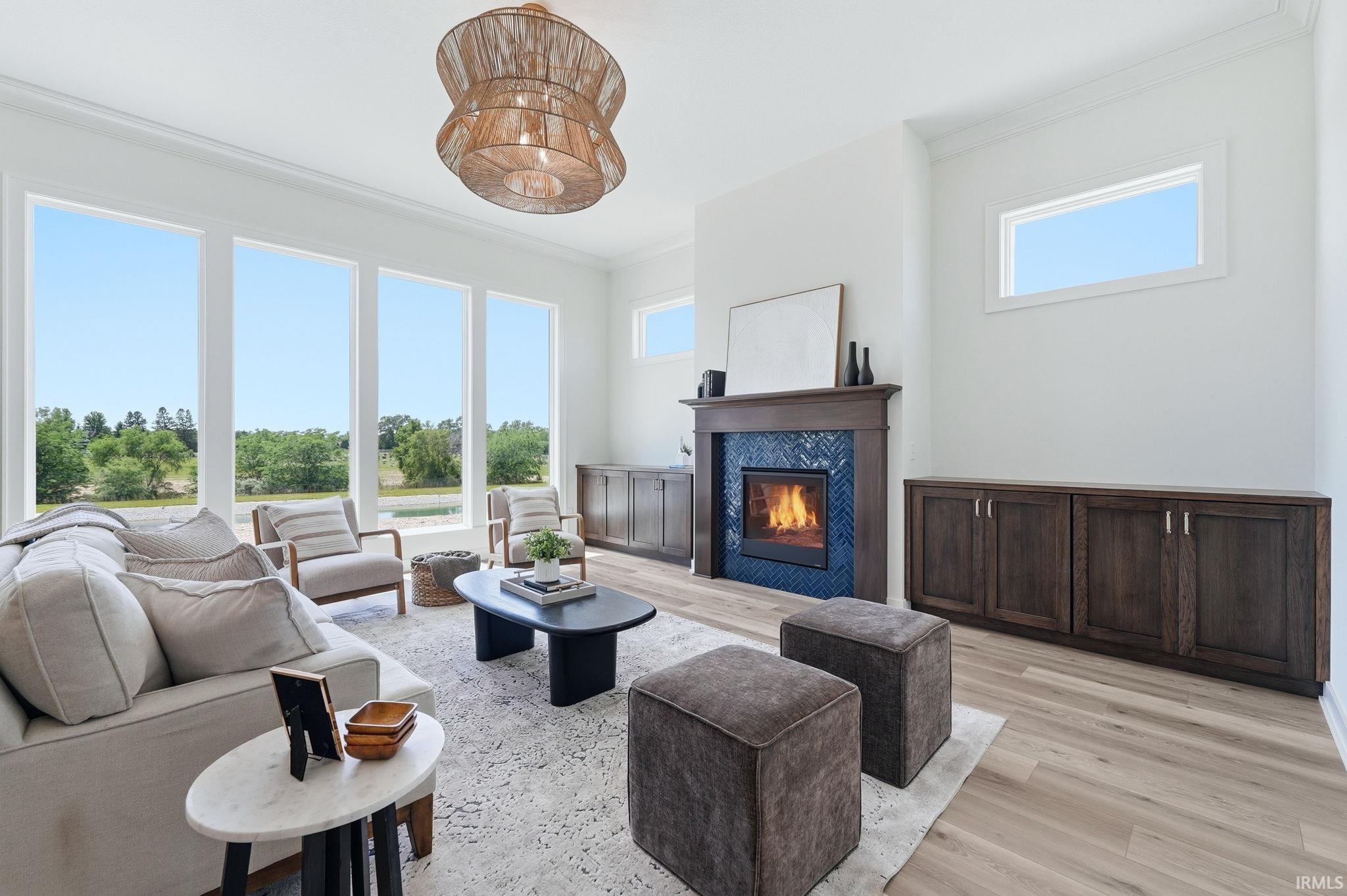 Living area featuring a fireplace with a wood mantel and blue tile surround, built-in wood cabinetry, wood-finish flooring, and multiple large windows