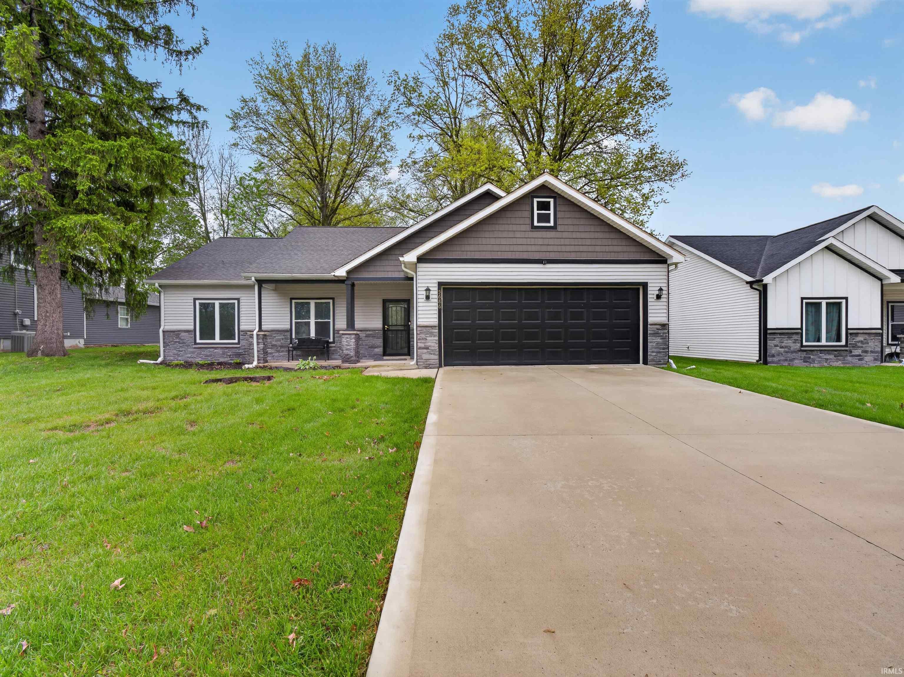 Contemporary ranch-style exterior featuring a dark gray roof, two-tone siding with stone veneer accents, a dark gray garage door, and a concrete driveway
