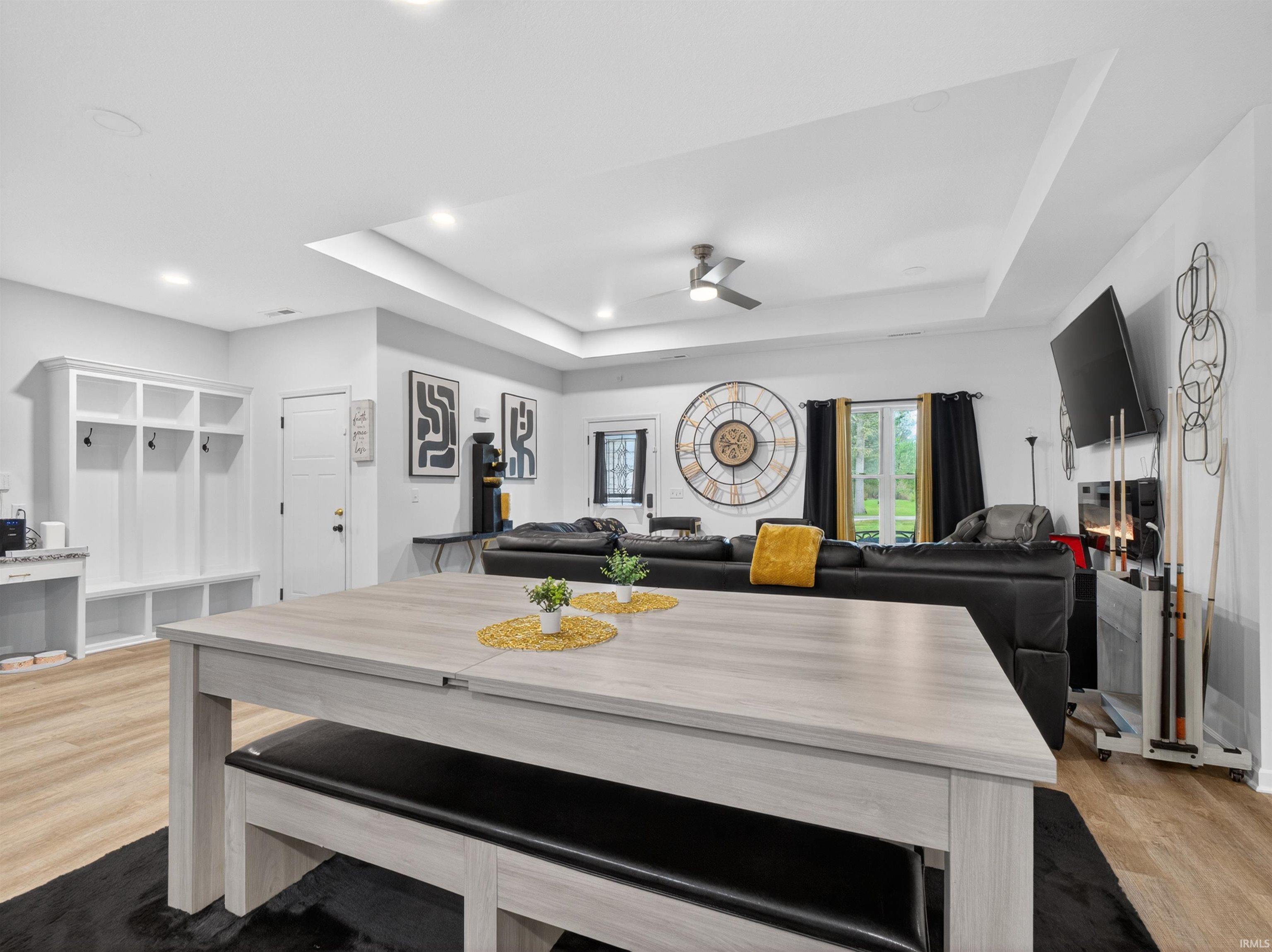 Open-concept living area featuring light wood-finish flooring, recessed lighting, a tray ceiling, and a built-in hall tree with storage cubbies and hooks