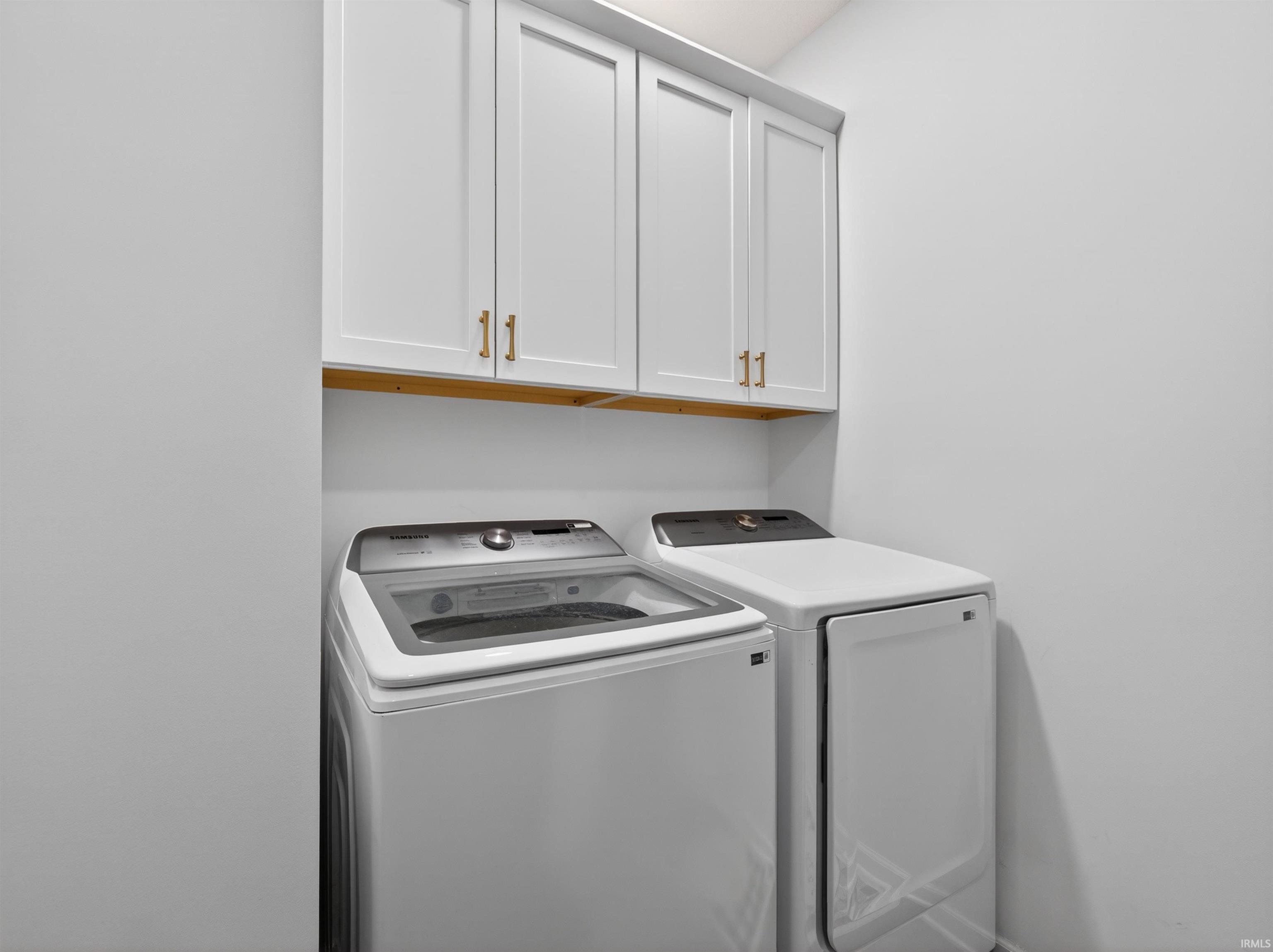 Laundry area featuring white shaker-style cabinetry with gold-tone hardware, a wood-finish shelf, and light-toned walls