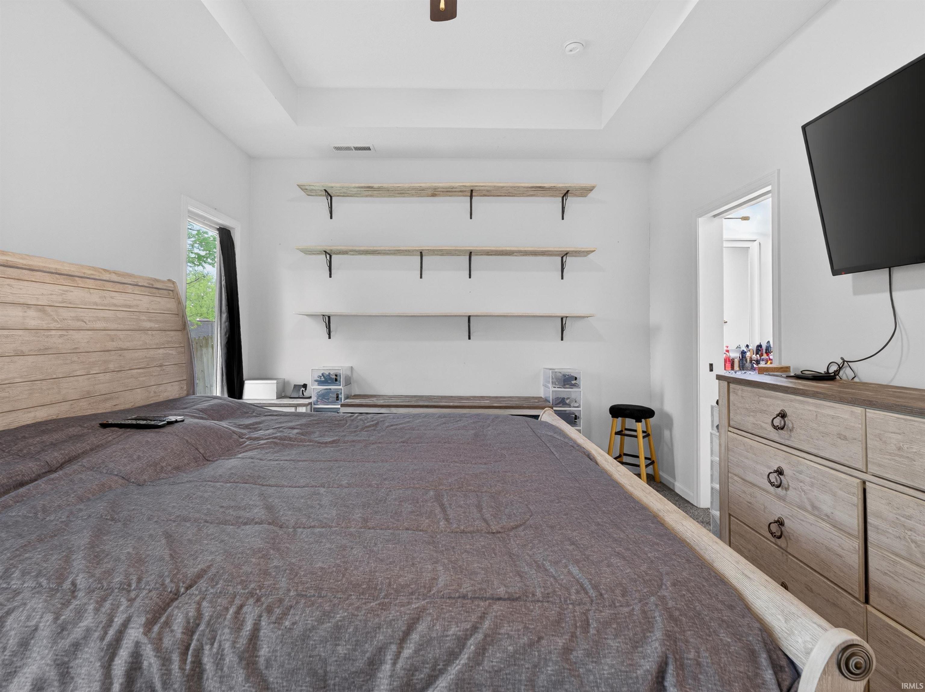 Room featuring a tray ceiling, three wall-mounted shelves, and a window with black privacy drapes
