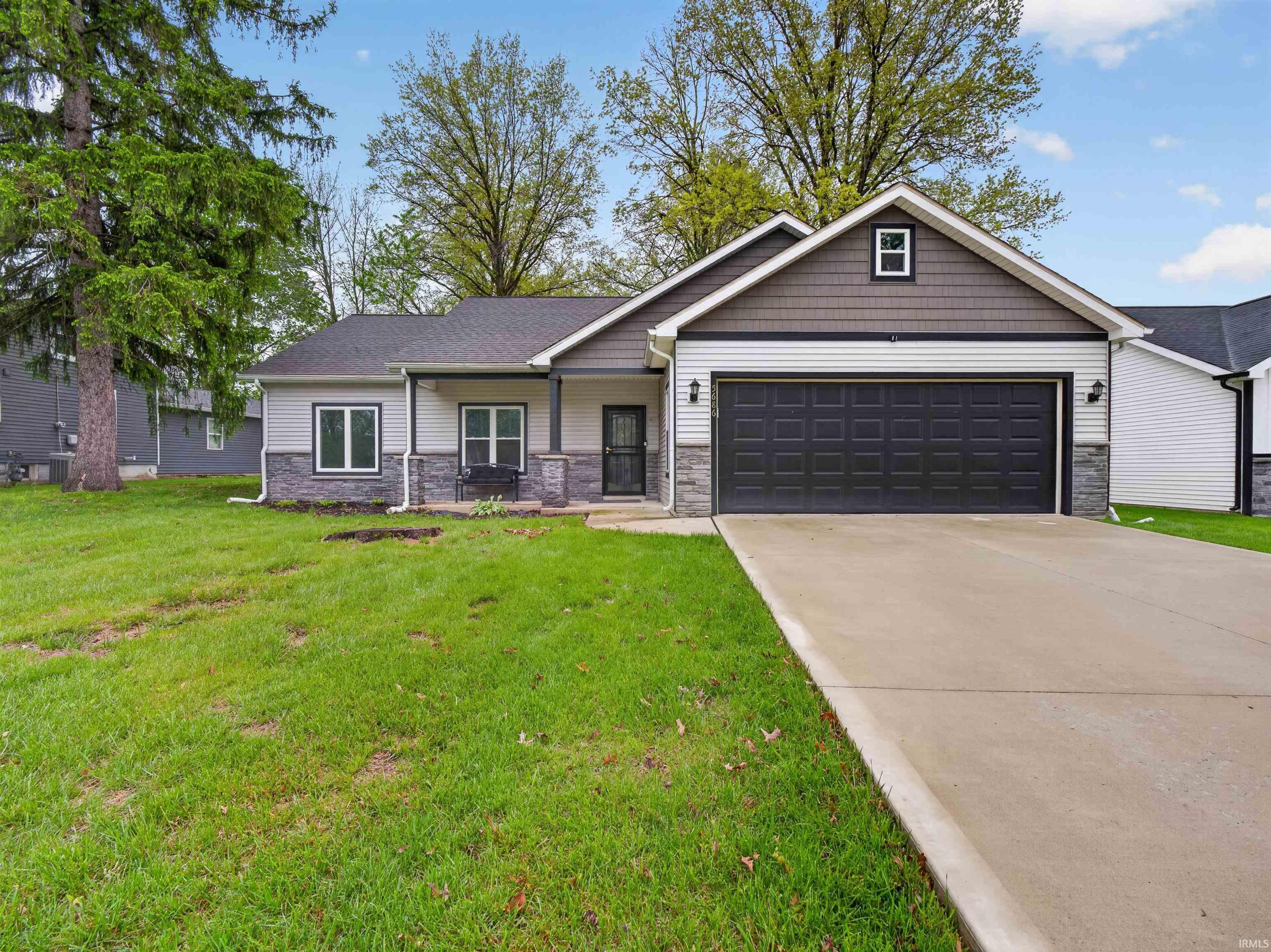 Exterior featuring a dark gray paneled garage door, light gray siding, dark gray shingle roofing, dark gray stone accenting, and a concrete driveway