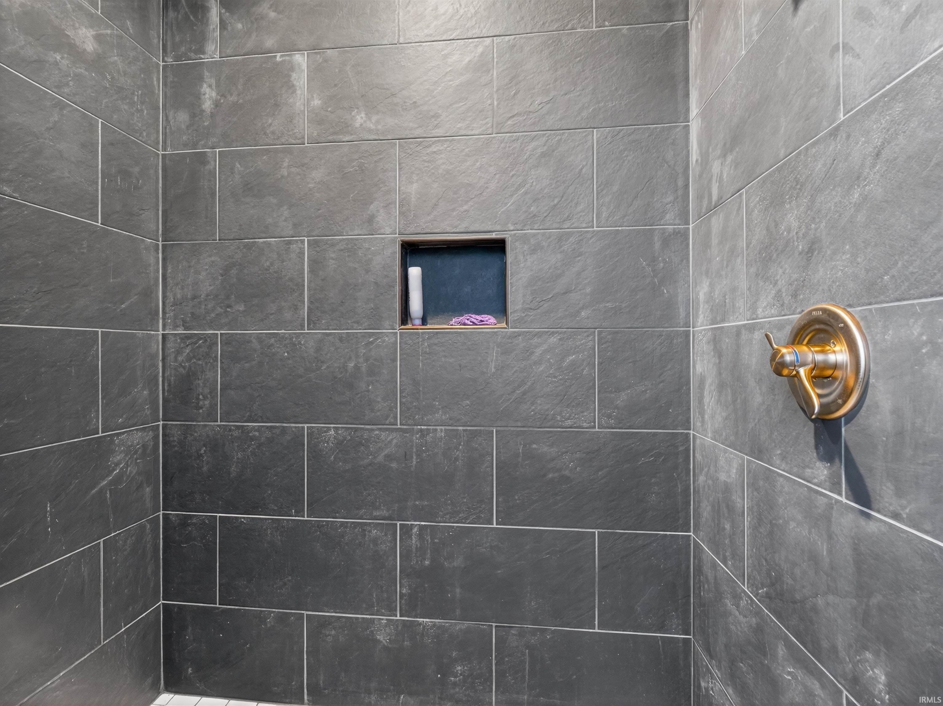 Shower enclosure featuring large format dark grey wall tiles, a built-in shower niche, and a brass-tone shower fixture