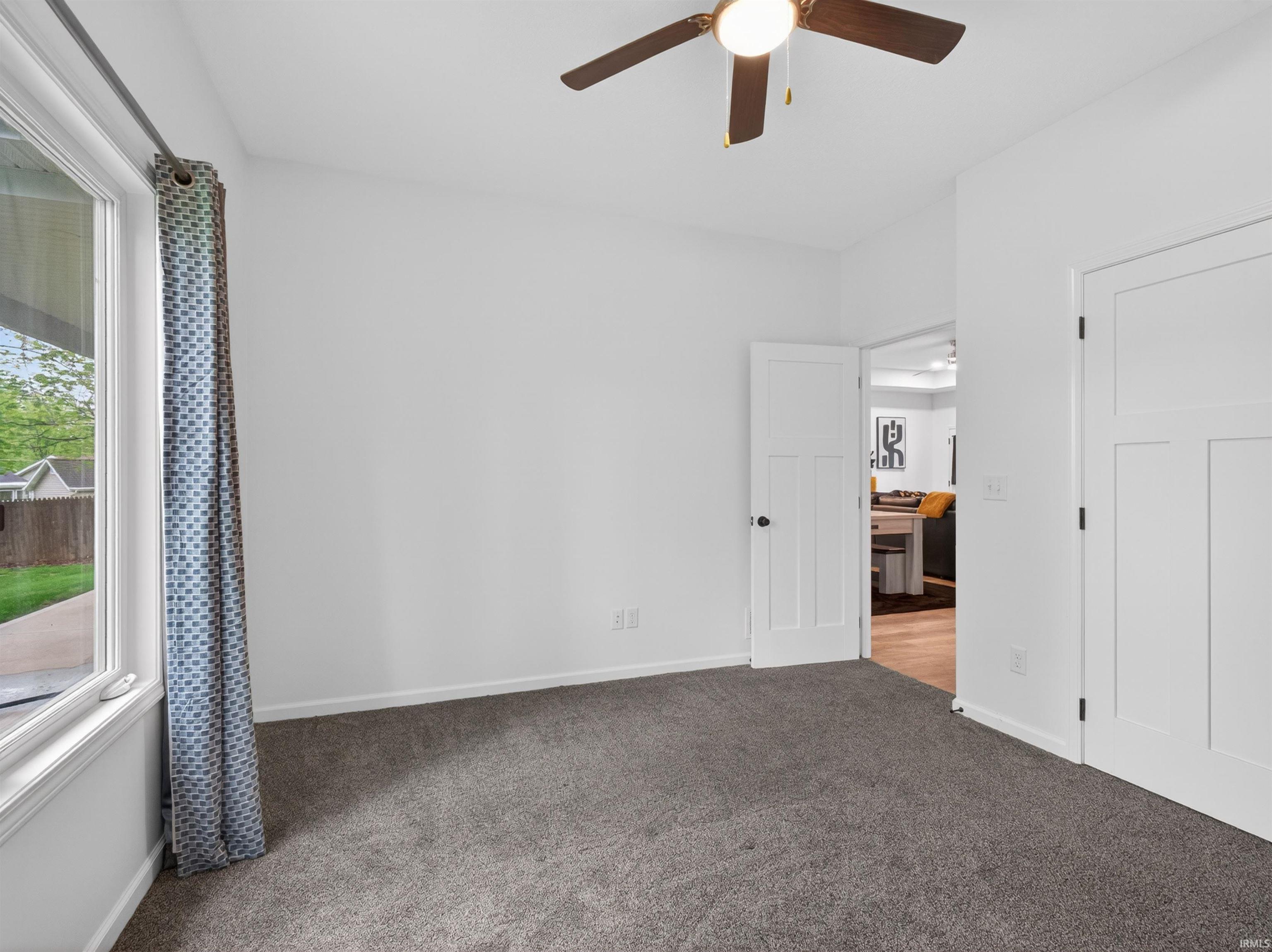 Interior room featuring neutral wall paint, gray carpet flooring, and a ceiling fan with integrated lighting