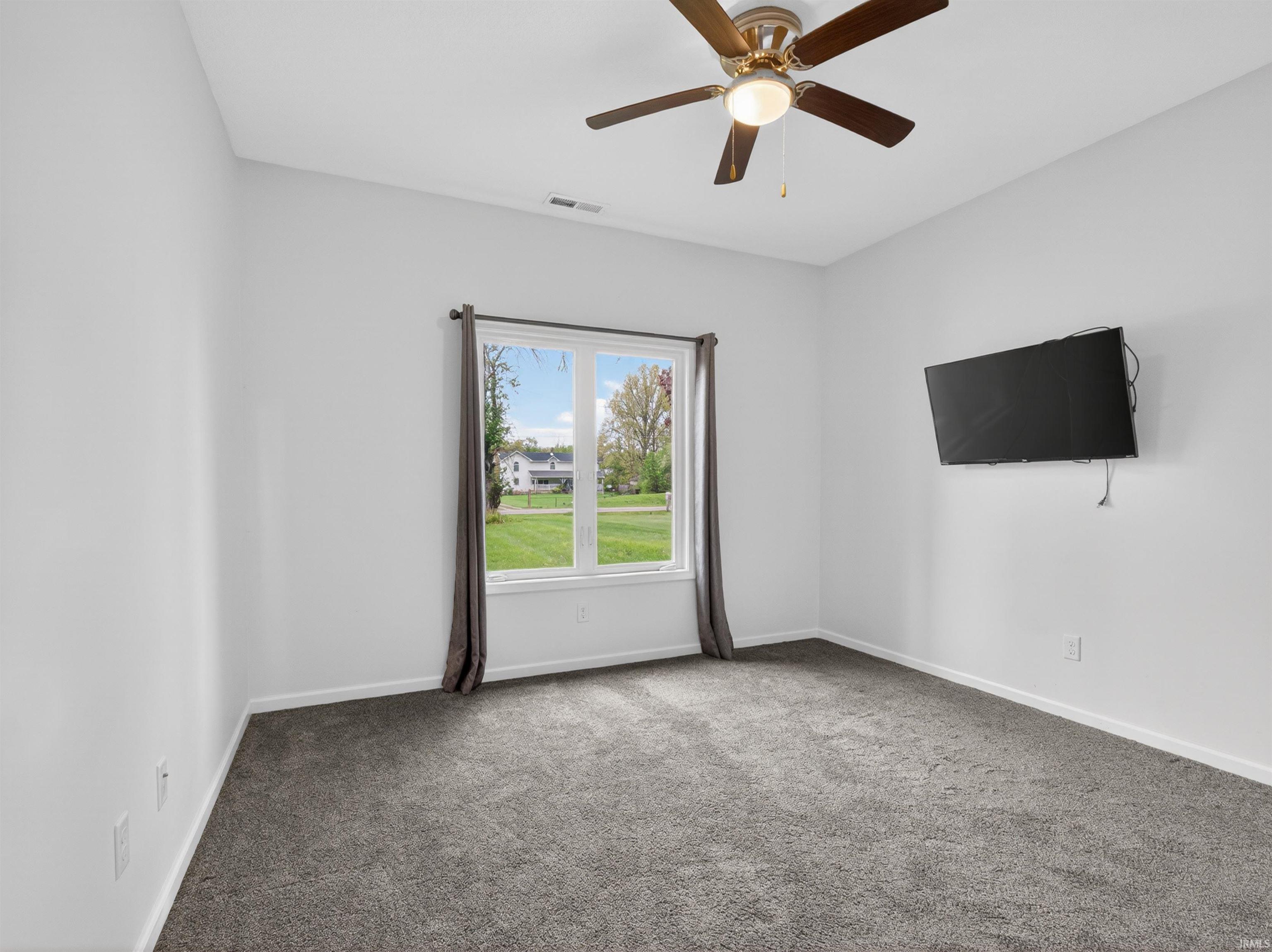 Carpeted room featuring a white-framed window, a ceiling fan with integrated lighting, and white walls
