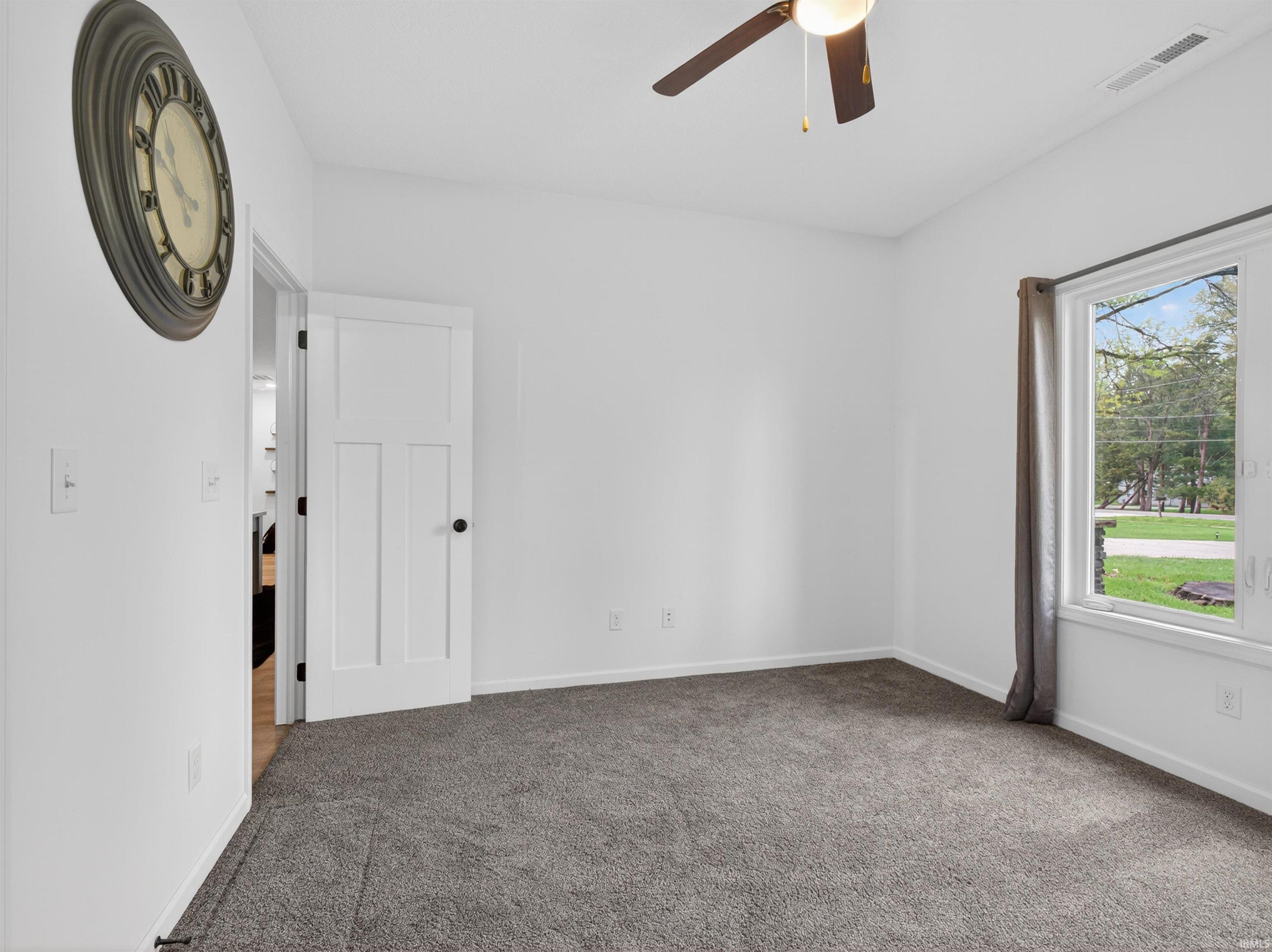 Carpeted room featuring a white interior door, a ceiling fan with integrated lighting, and a window with gray drapes