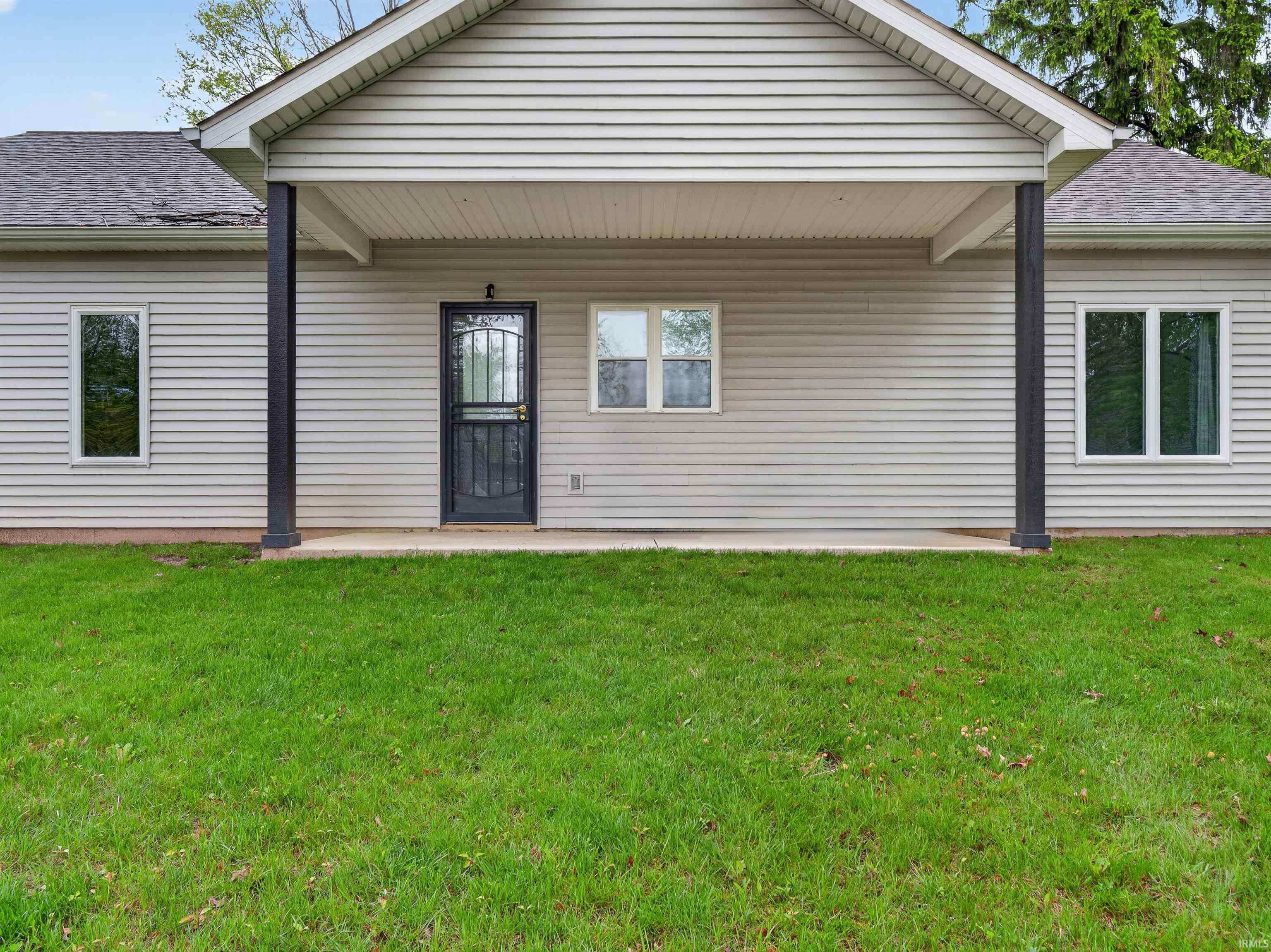 Front exterior featuring light-colored horizontal siding, a covered entry with dark support columns, a dark security screen door, and multiple windows