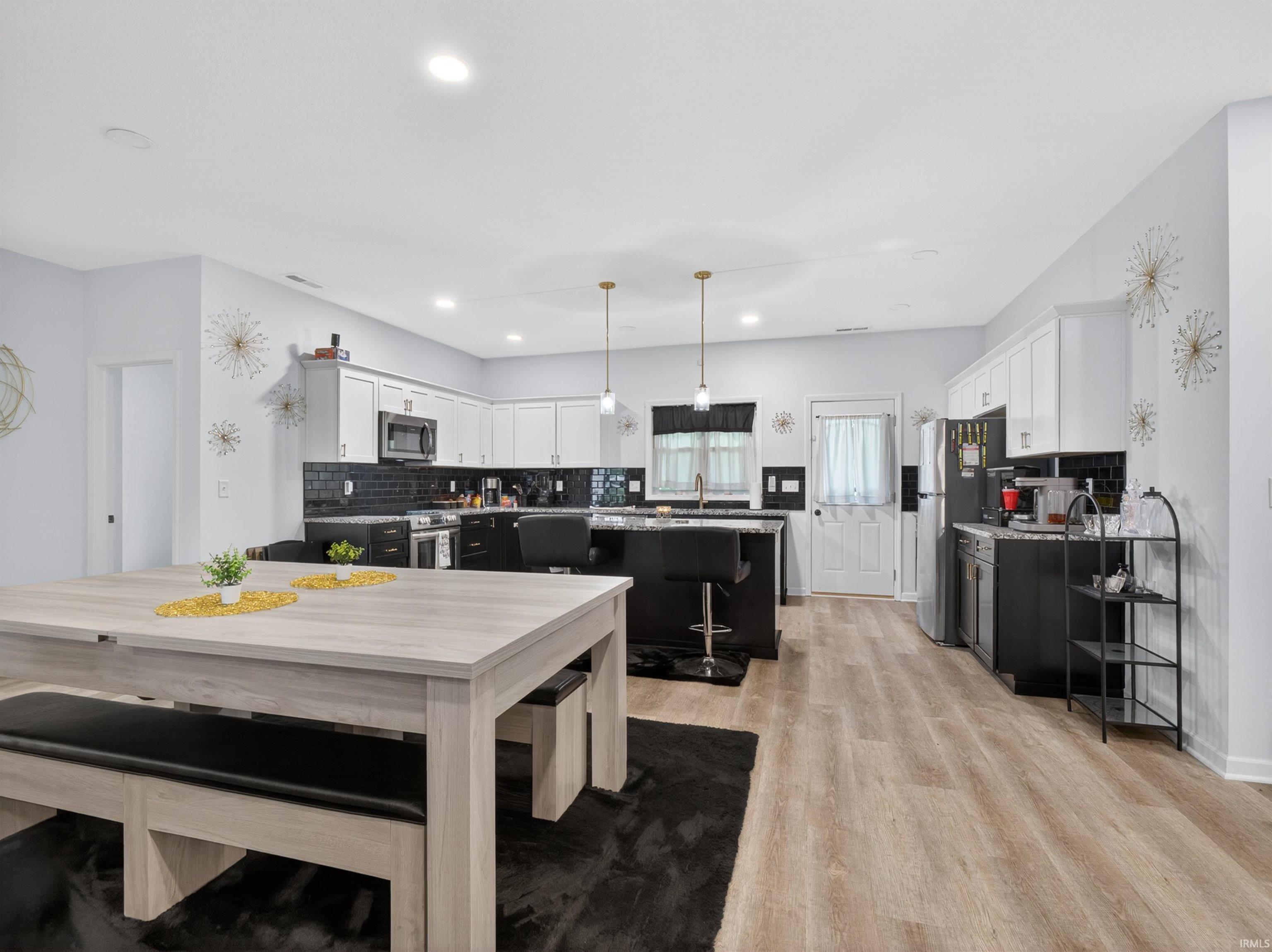 Open-concept kitchen featuring wood-finish flooring, white upper cabinetry, black lower cabinetry, and a dark tile backsplash