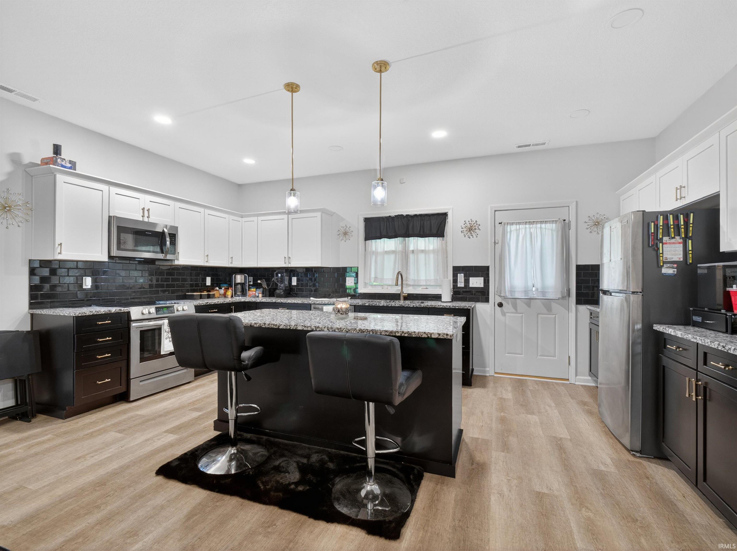 Kitchen featuring a central island with a granite-style countertop, recessed lighting, wood-finish flooring, white upper cabinetry, and dark subway tile backsplash