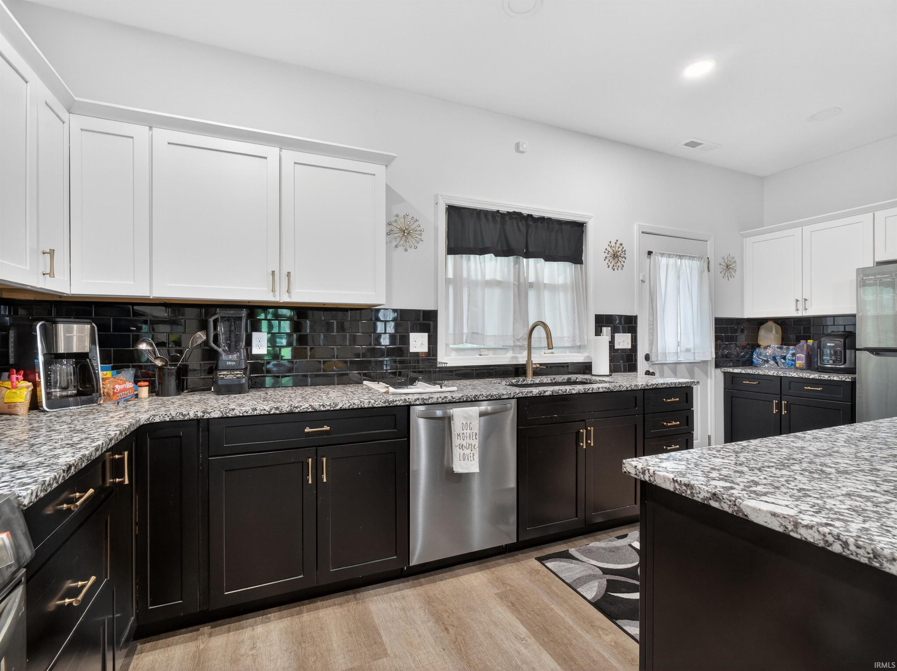 Kitchen featuring two-tone cabinetry, granite countertops, and a black subway tile backsplash