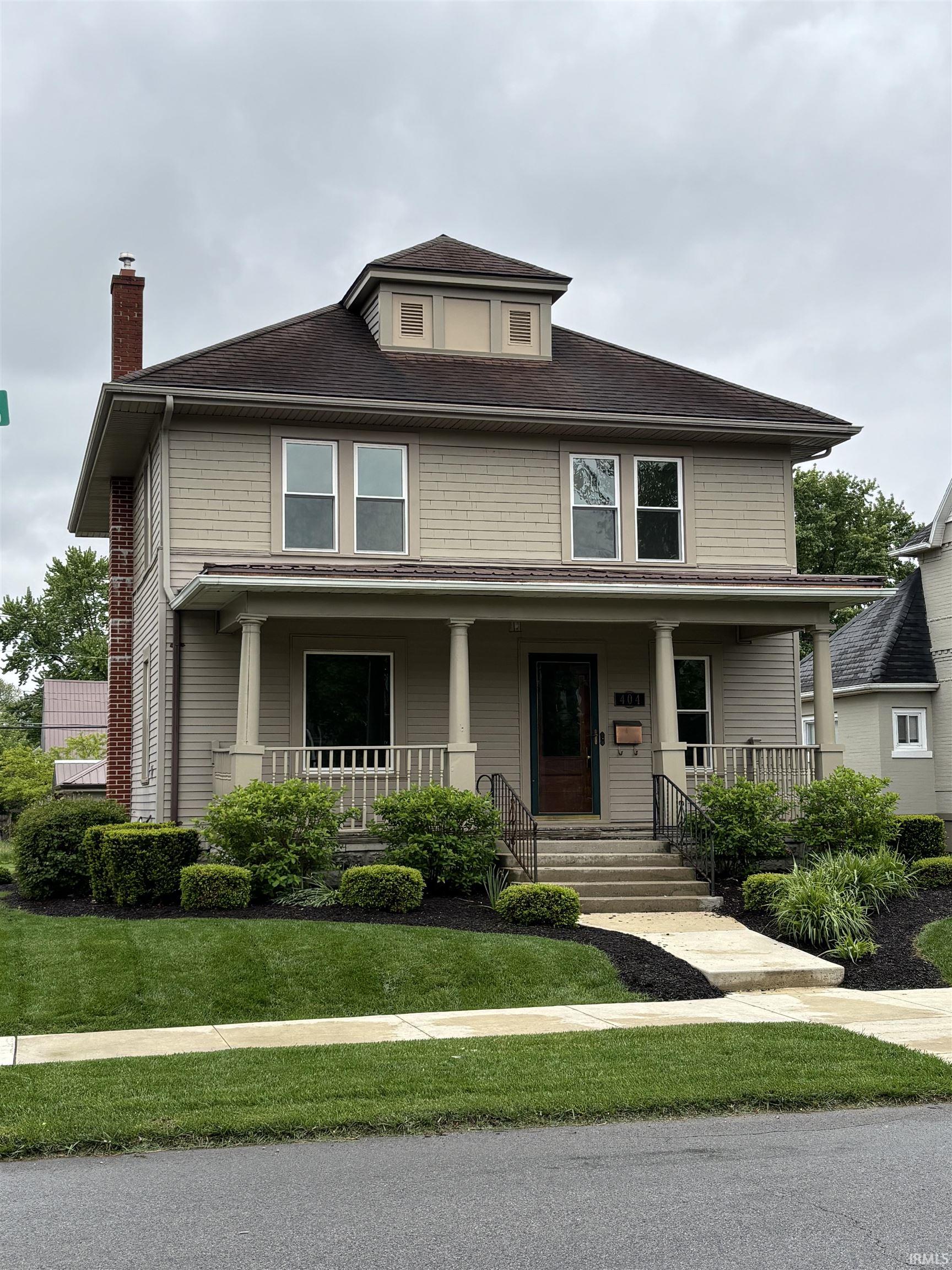 Traditional home exterior featuring a front porch with columns, a dormer, and a brick chimney