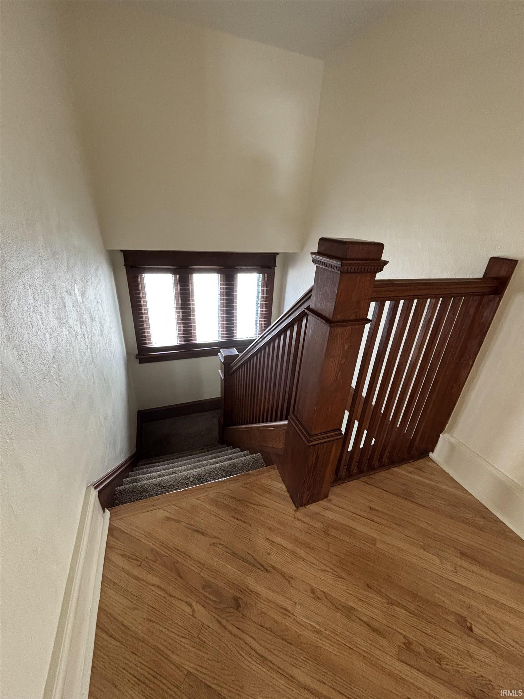 Staircase featuring wood-finish flooring, a dark wood newel post and balusters, and carpeted treads