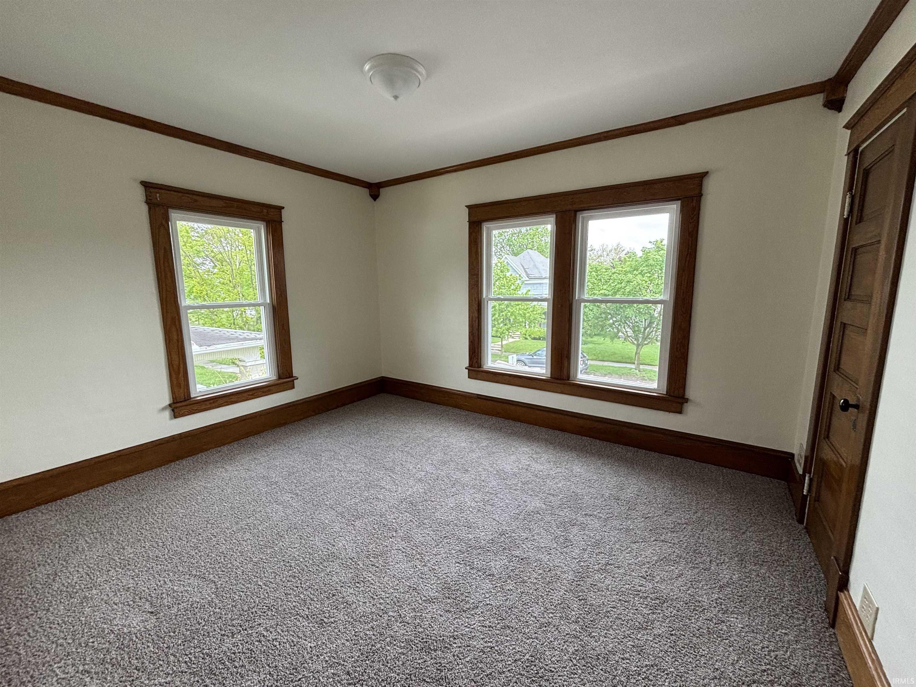 Room featuring light tan carpet, multiple windows with natural wood trim, a natural wood paneled door, and a flush-mount ceiling light fixture
