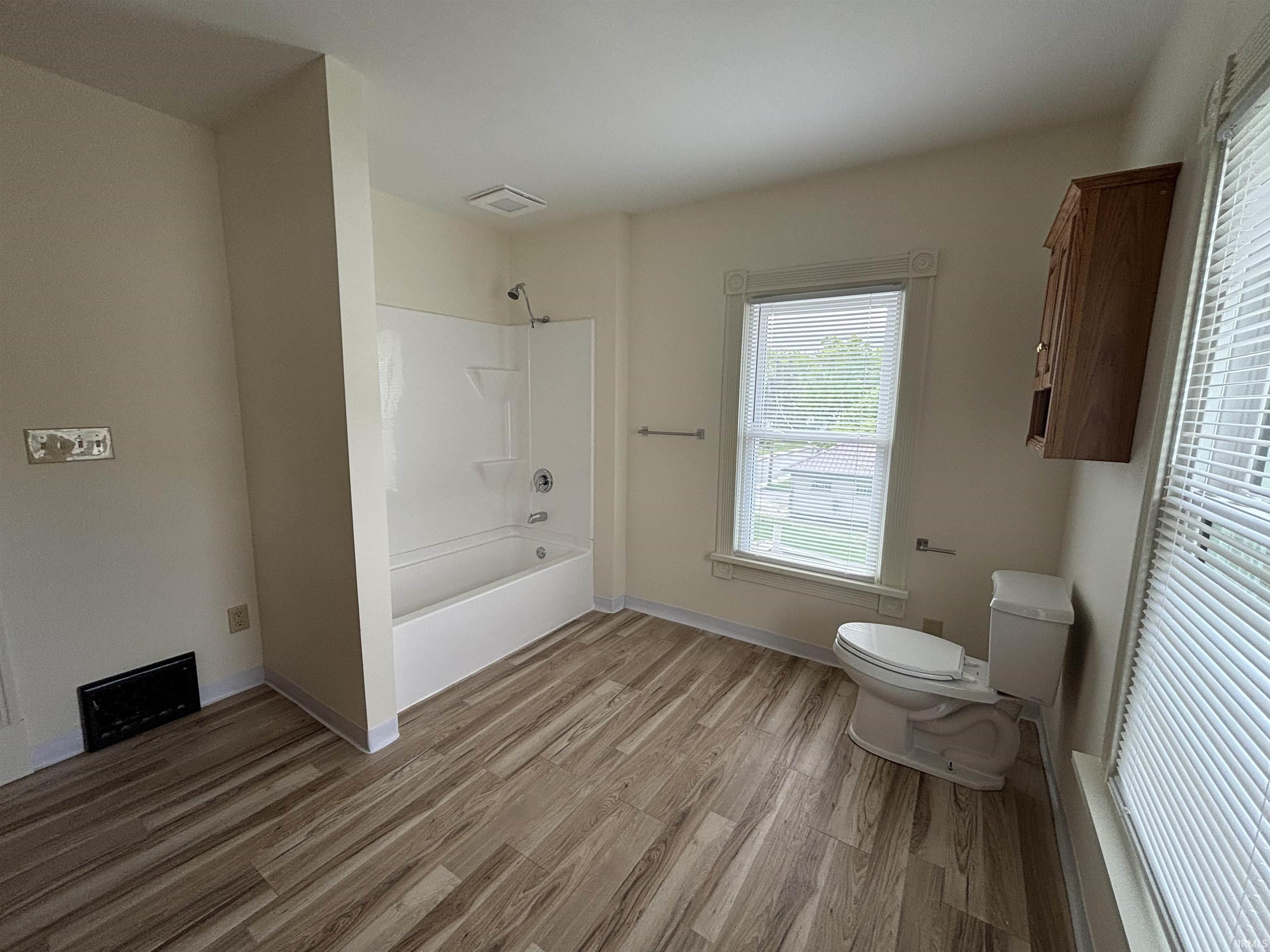 Wood-finish flooring throughout, a white tub and shower combination