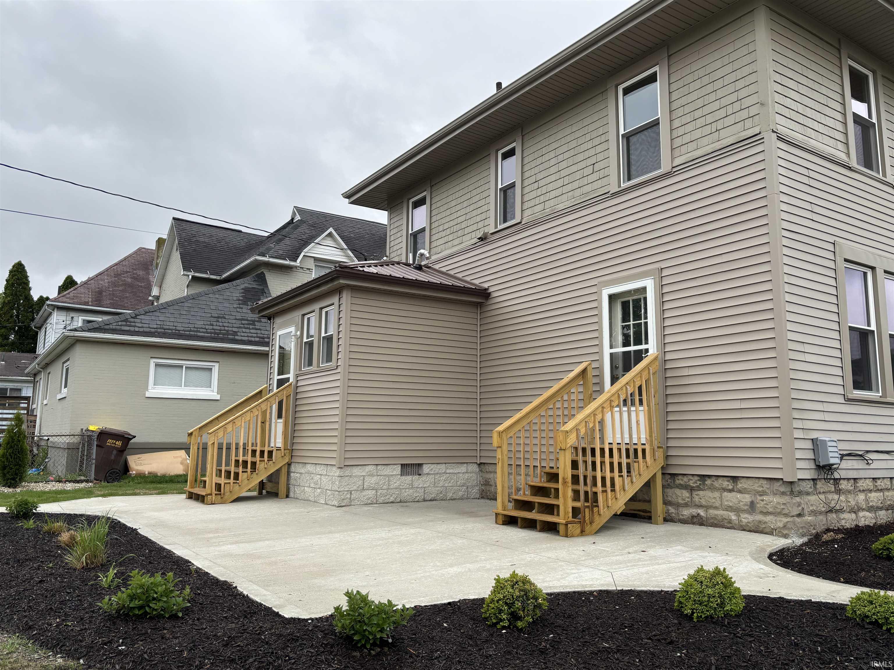 Rear exterior featuring tan horizontal siding and shake siding on the upper level with new concrete patio and landscaping
