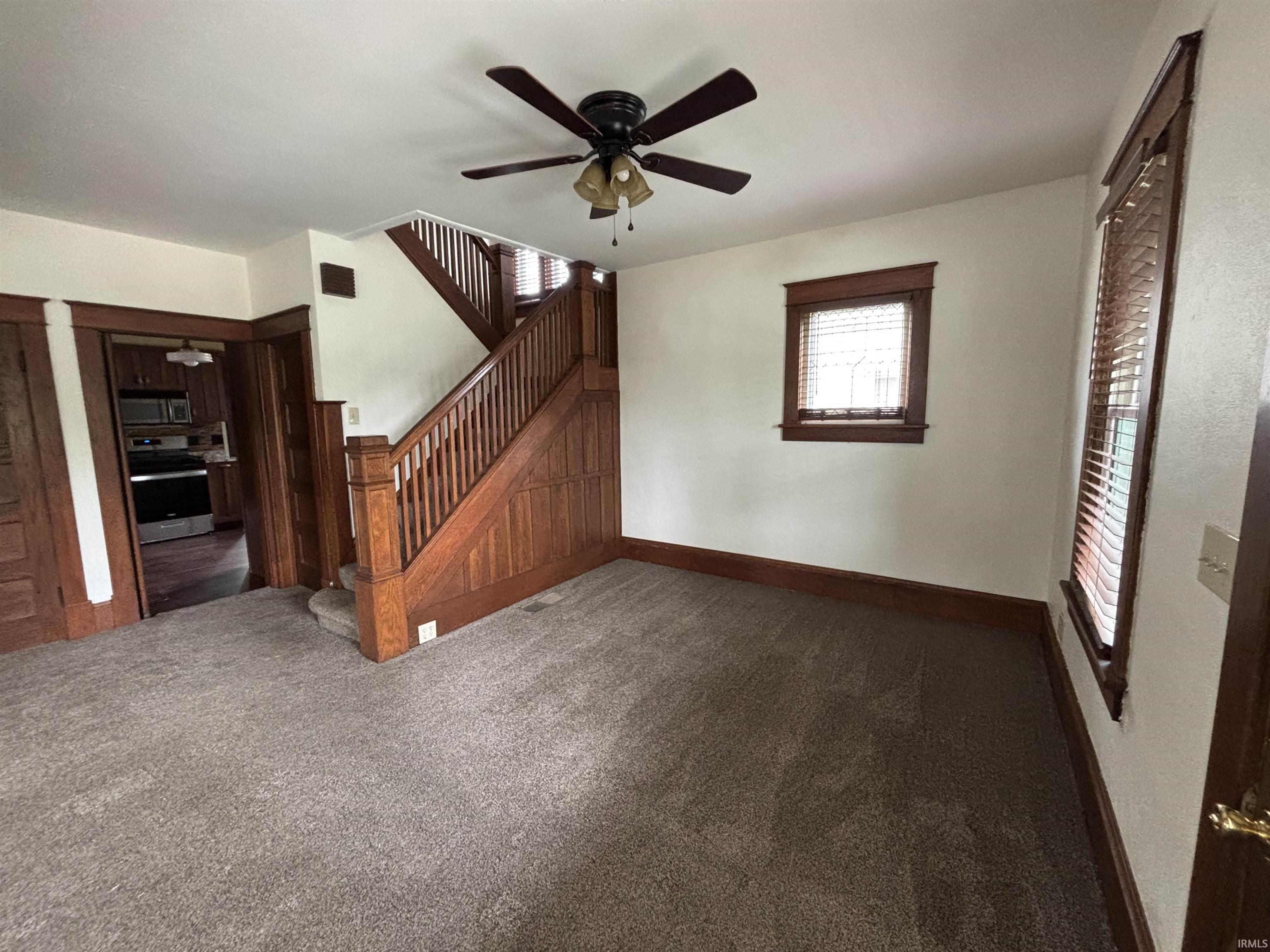 Living area featuring a grand staircase with rich wood finishes, neutral carpet flooring, and a ceiling fan