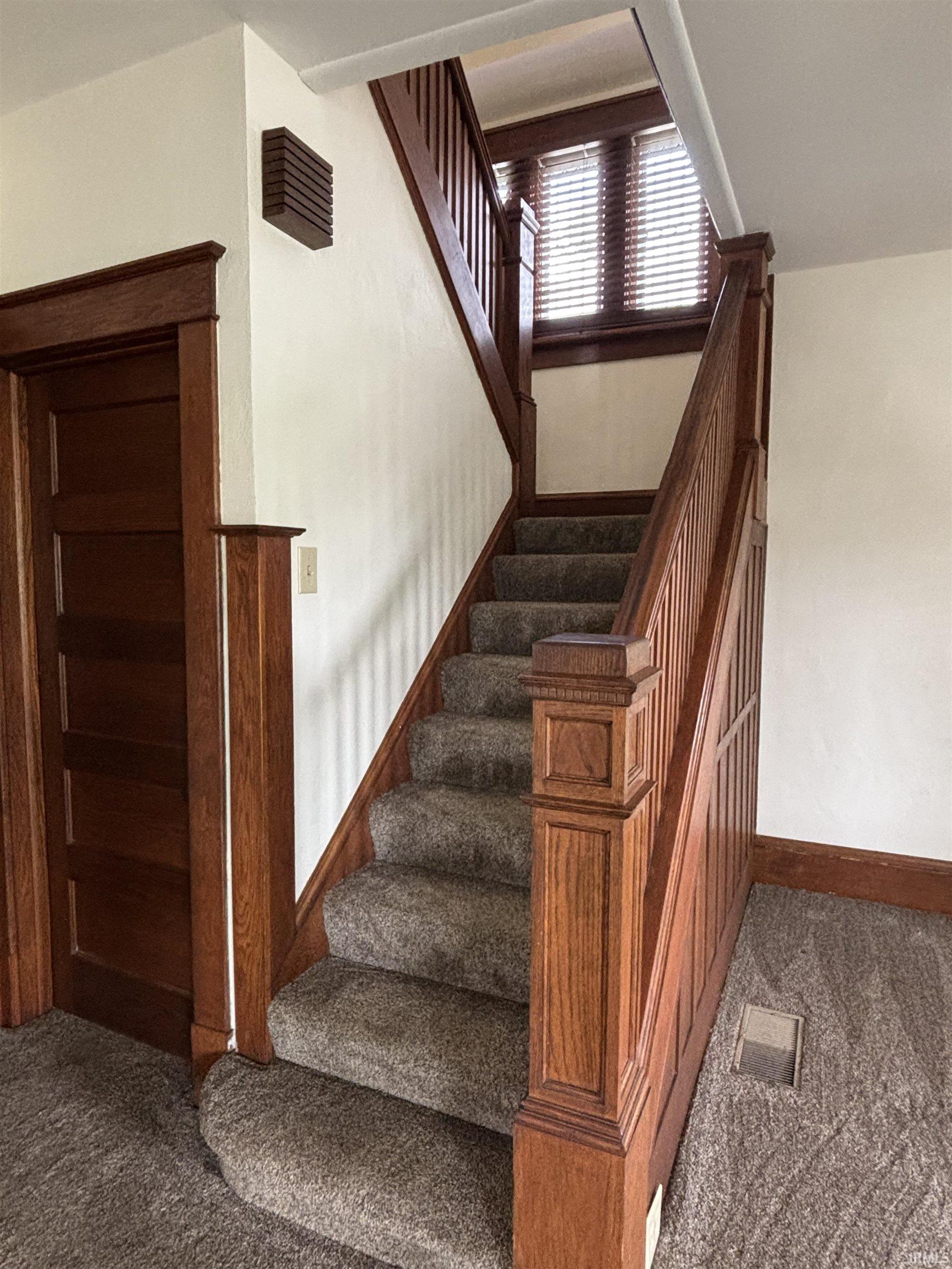 Carpeted staircase featuring wood-finish railings, newel posts, and trim