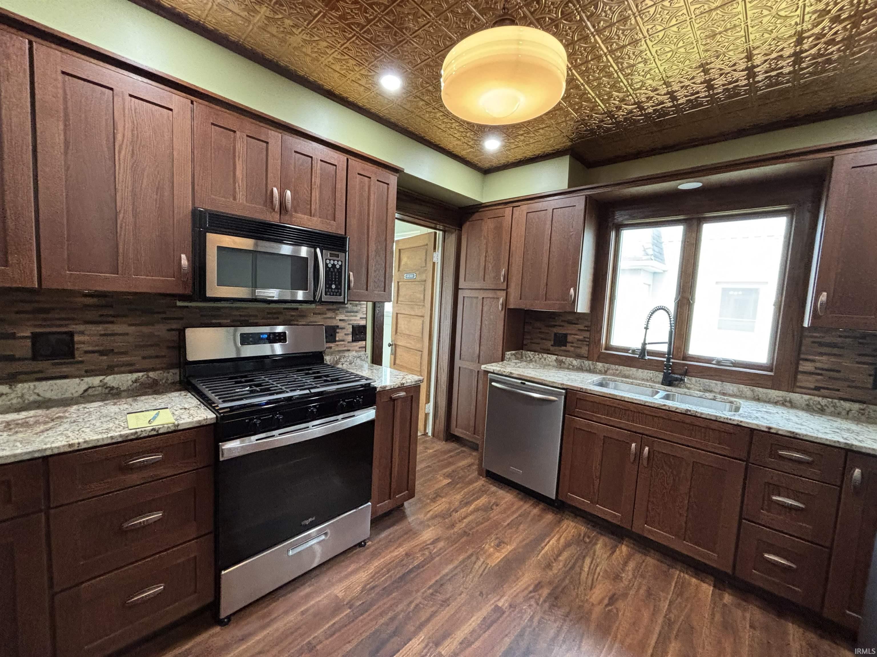 Kitchen featuring a pressed tin ceiling, wood-finish flooring, granite countertops, stainless steel appliances, and wood cabinetry