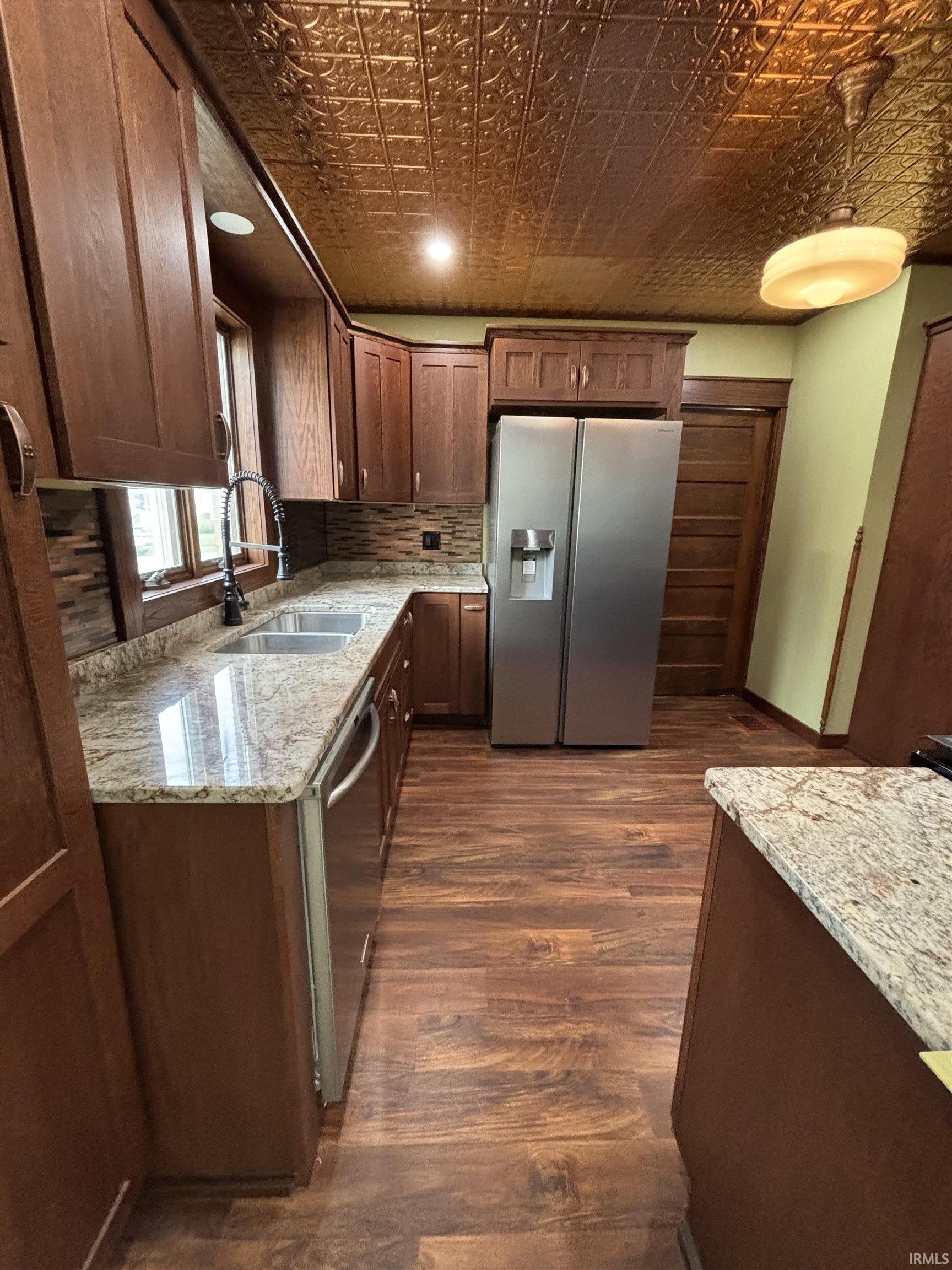 Kitchen featuring a copper-tone pressed tin ceiling, wood-finish flooring, granite countertops, and stainless steel appliances