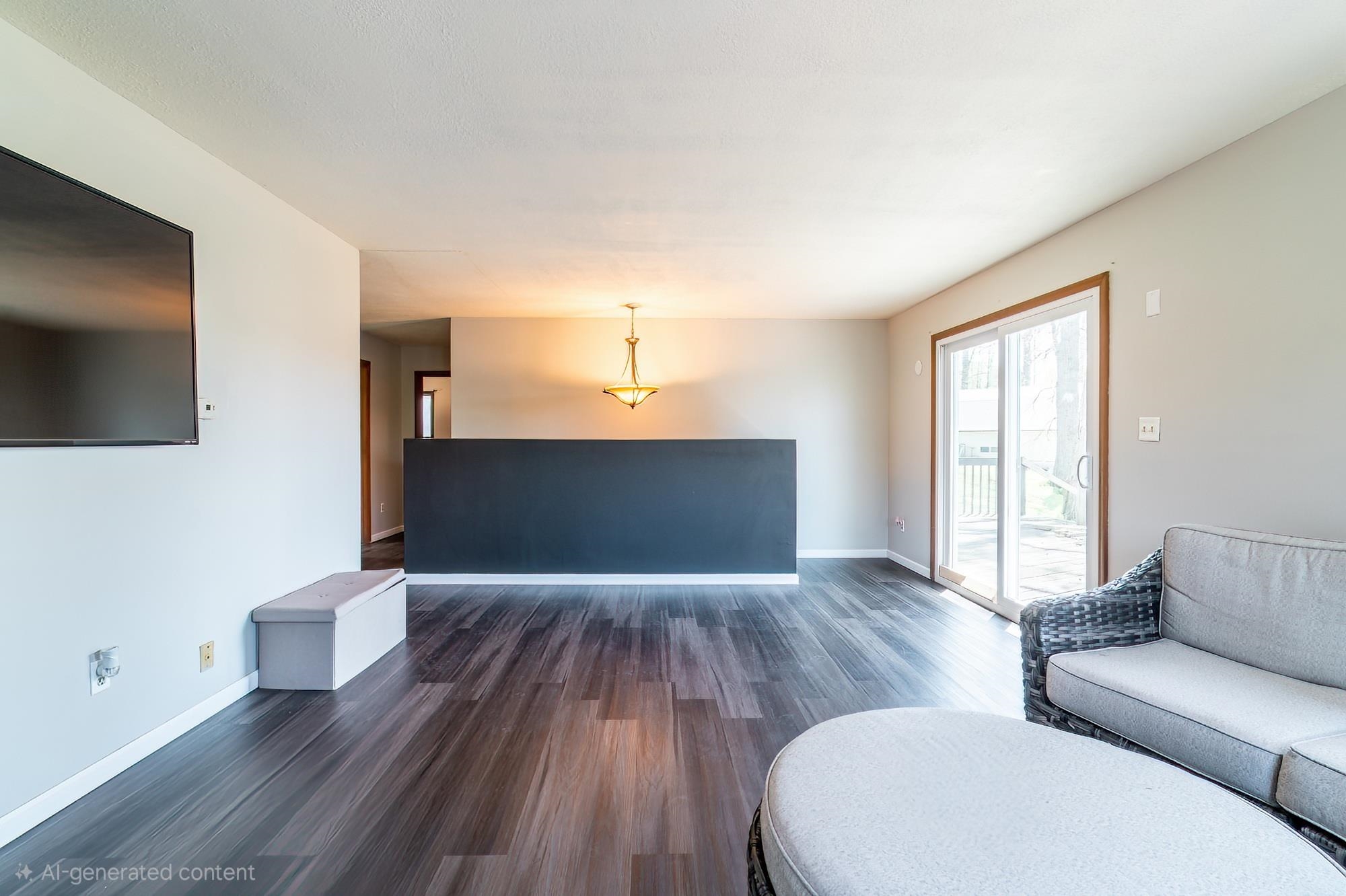 Spacious living area featuring wood-finish flooring, a contemporary light fixture, and a sliding glass door providing direct outdoor access