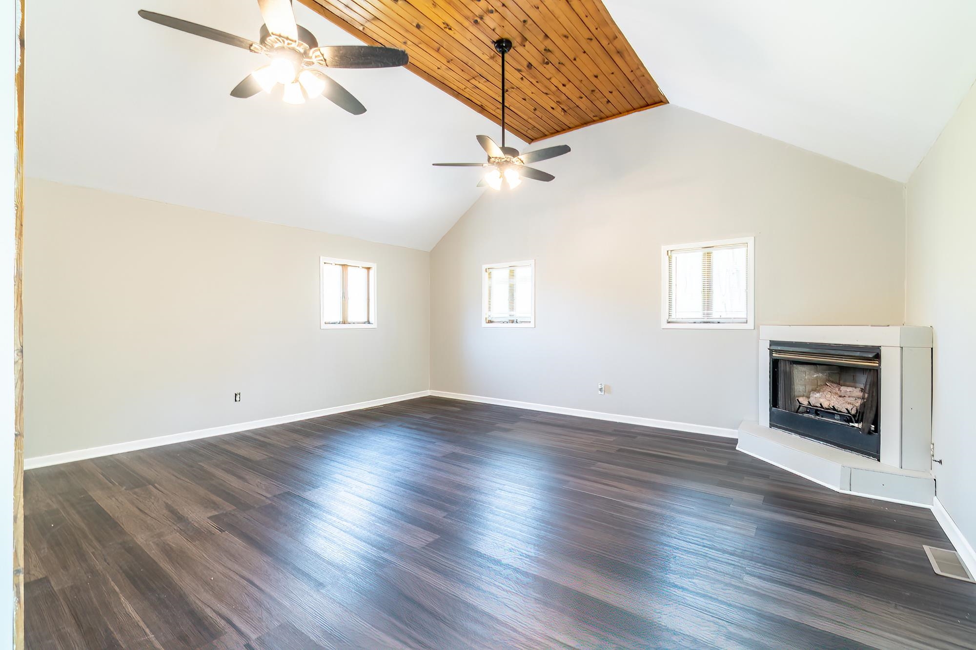 Spacious room featuring vaulted ceilings with wood paneling accents and two ceiling fans