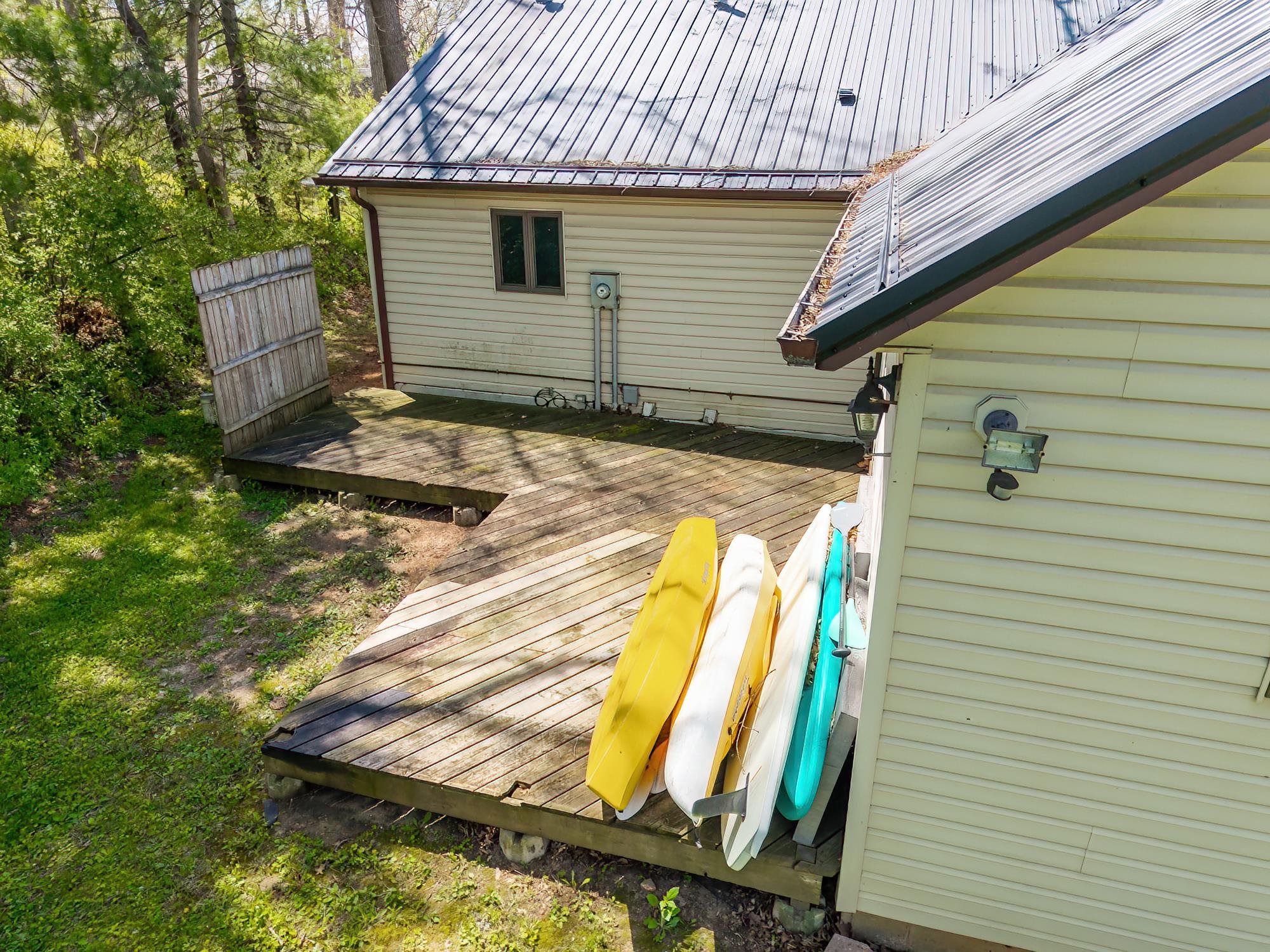 Two-level wood-finish deck with a privacy fence, positioned at the rear of a cream-colored siding structure with a metal roof