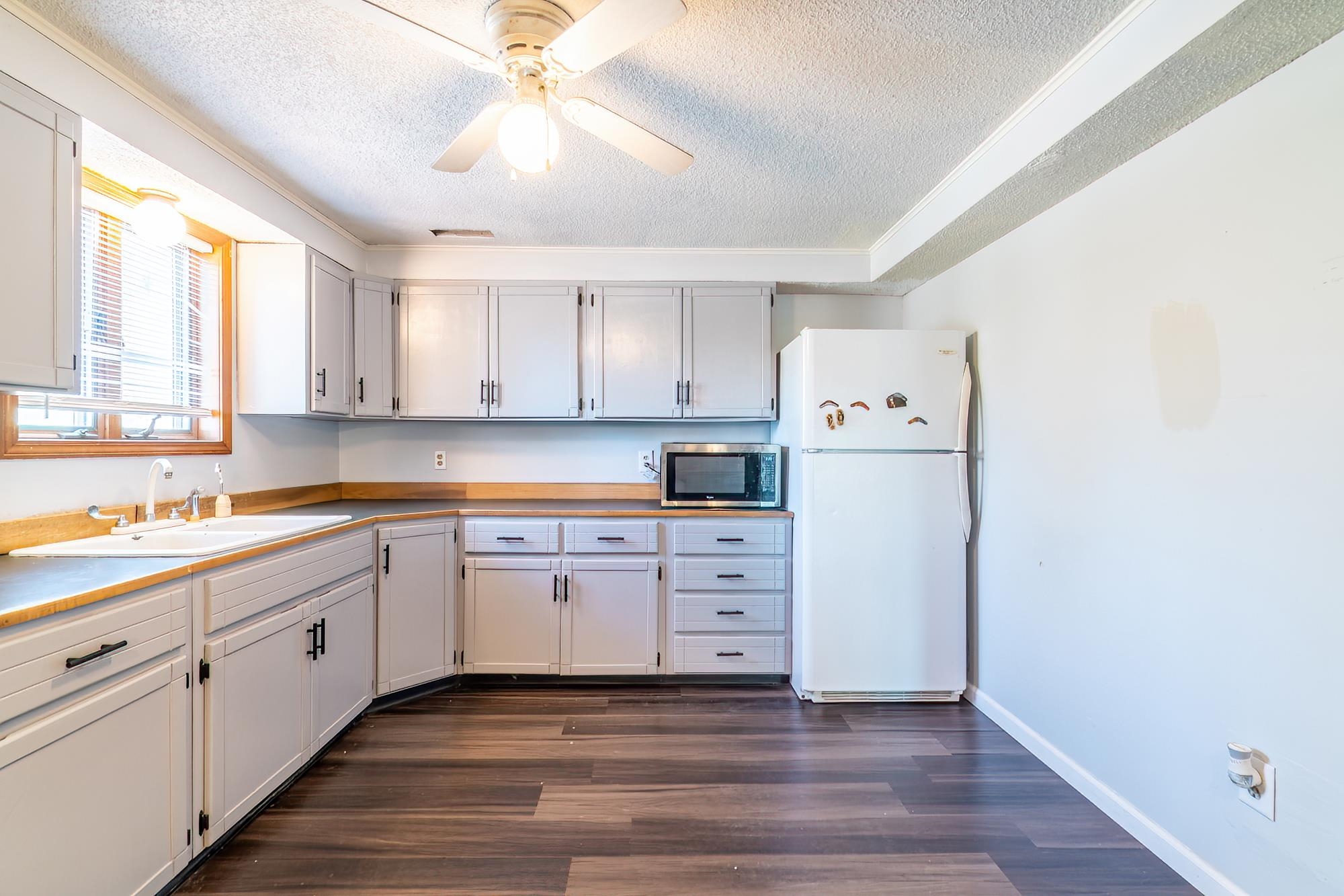 Kitchen featuring L-shaped cabinetry, wood-finish flooring, a double basin sink, and a ceiling fan with integrated lighting